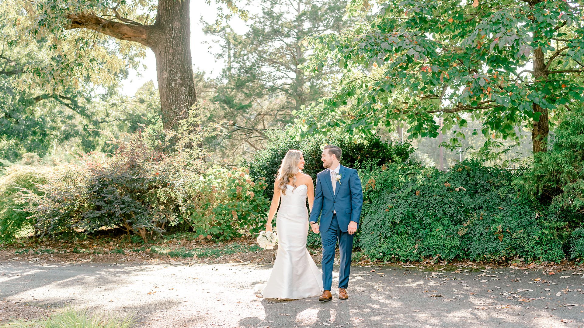 Bride and groom walking hand-in-hand along garden path surrounded by lush greenery at Charlotte NC wedding venue