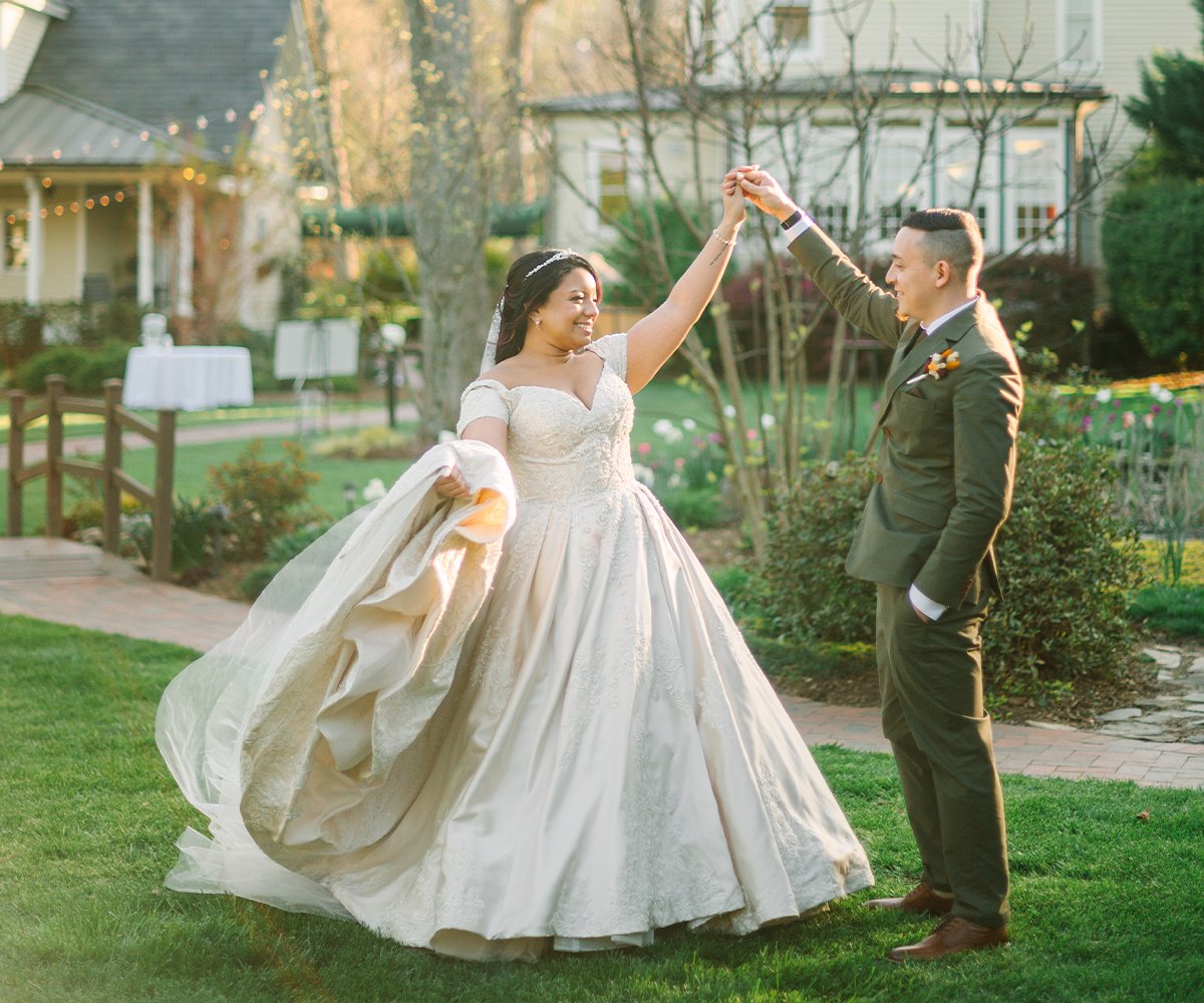 Couple in elegant wedding attire dancing on manicured lawn with historic Charlotte NC venue in background