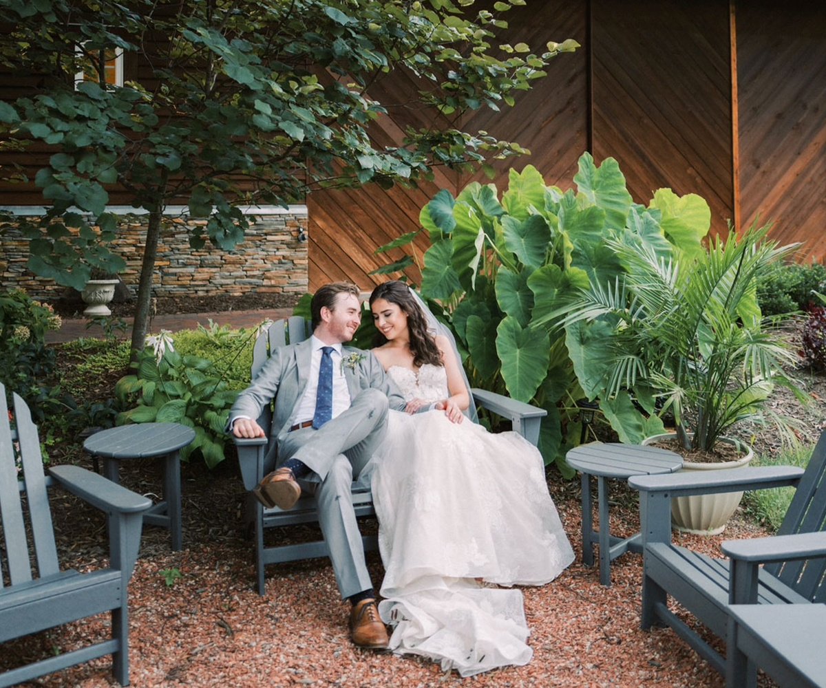 Intimate moment between newlyweds on Adirondack chairs surrounded by lush tropical plants at Charlotte wedding venue