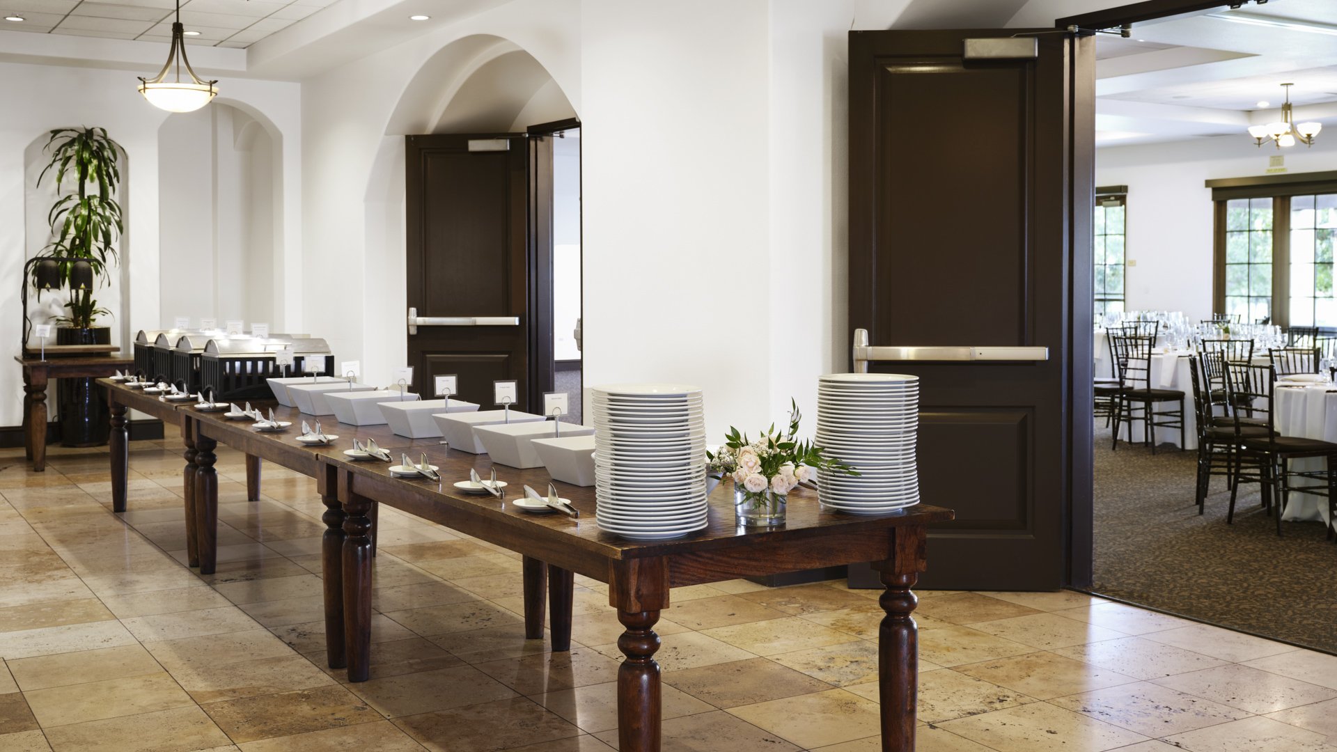 Elegant buffet service setup with wooden tables, white serving dishes, stacked plates, and floral arrangements at Aliso Viejo by Wedgewood Weddings California venue