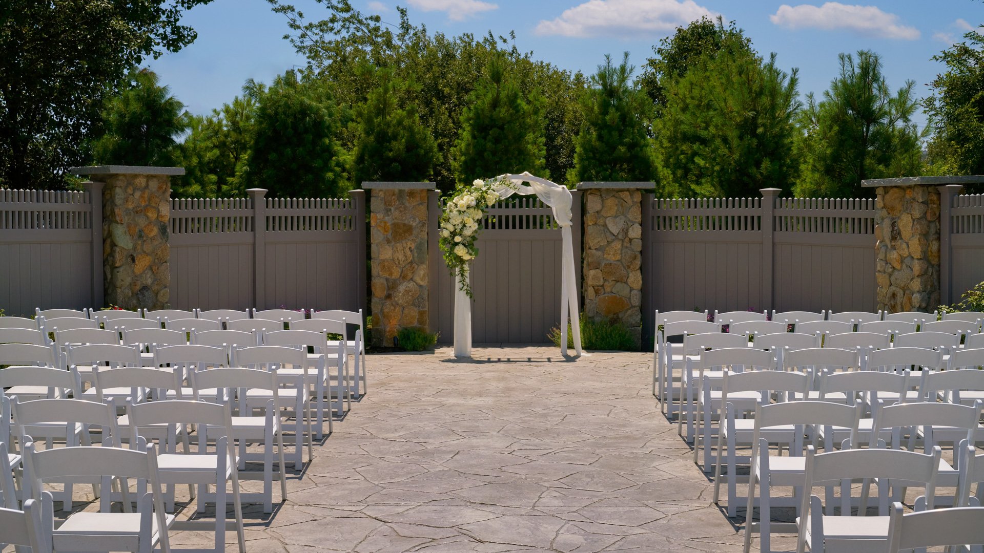 Floral-draped arbor set for an outdoor wedding ceremony in The Barker House garden courtyard, surrounded by greenery and natural stone accents.
