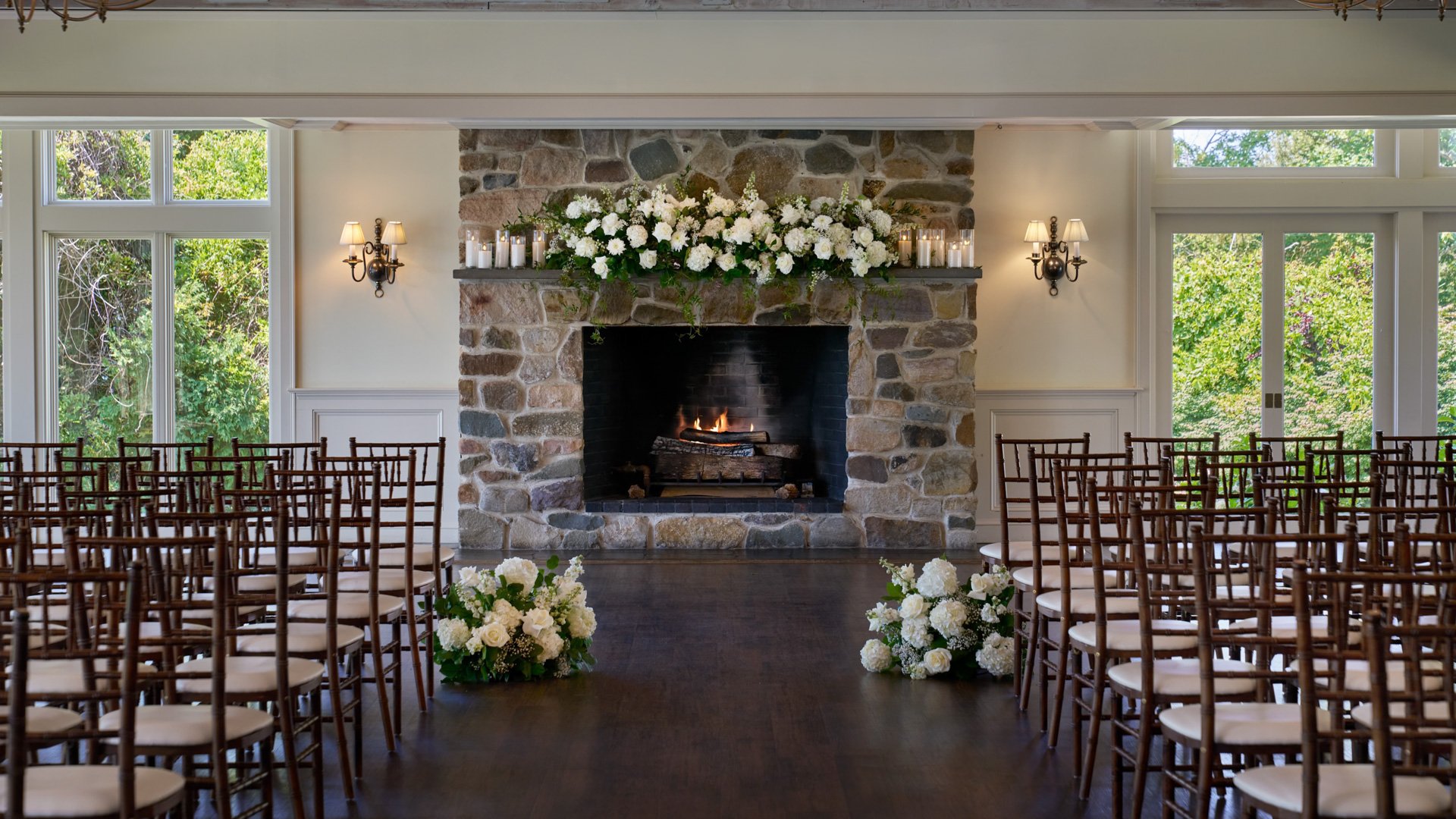 Close-up of the wedding ceremony altar inside The Barker House’s Williams Room, showcasing a rustic stone fireplace with white roses and hydrangeas.