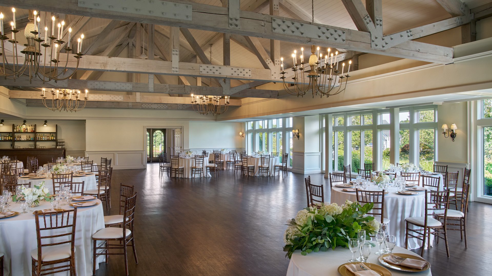 Elegant reception setup in The Barker House Williams Room featuring a full bar, wooden chandeliers, and tables set with fine glassware and floral décor.