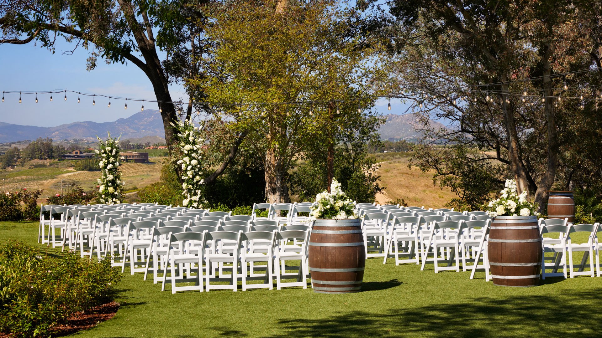 Outdoor wedding ceremony setup at Bel Vino Winery featuring white chairs, floral wine barrels, and sweeping vineyard scenery.