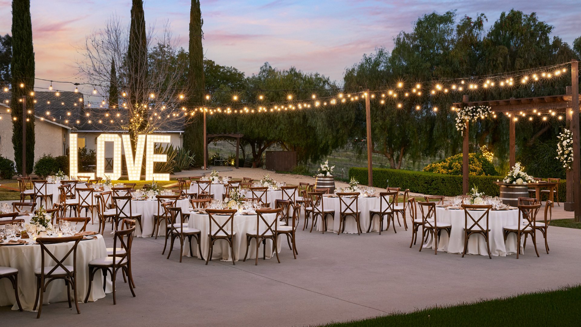 Outdoor wedding reception at Bel Vino Winery featuring illuminated LOVE sign, string lights, and elegant round tables.