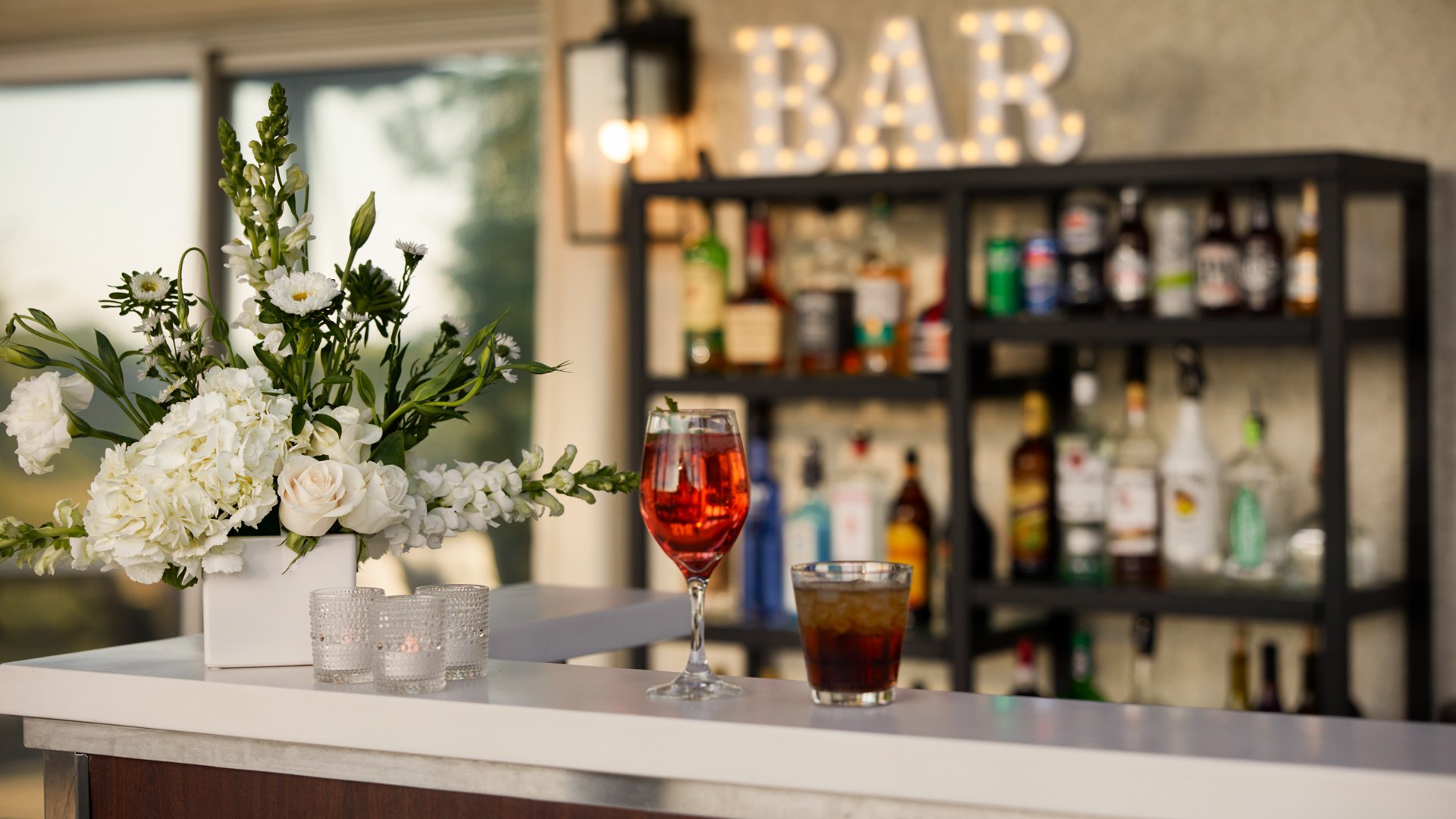 Close-up of bar setup at Bel Vino Winery featuring signature cocktails, floral décor, and illuminated bar sign.