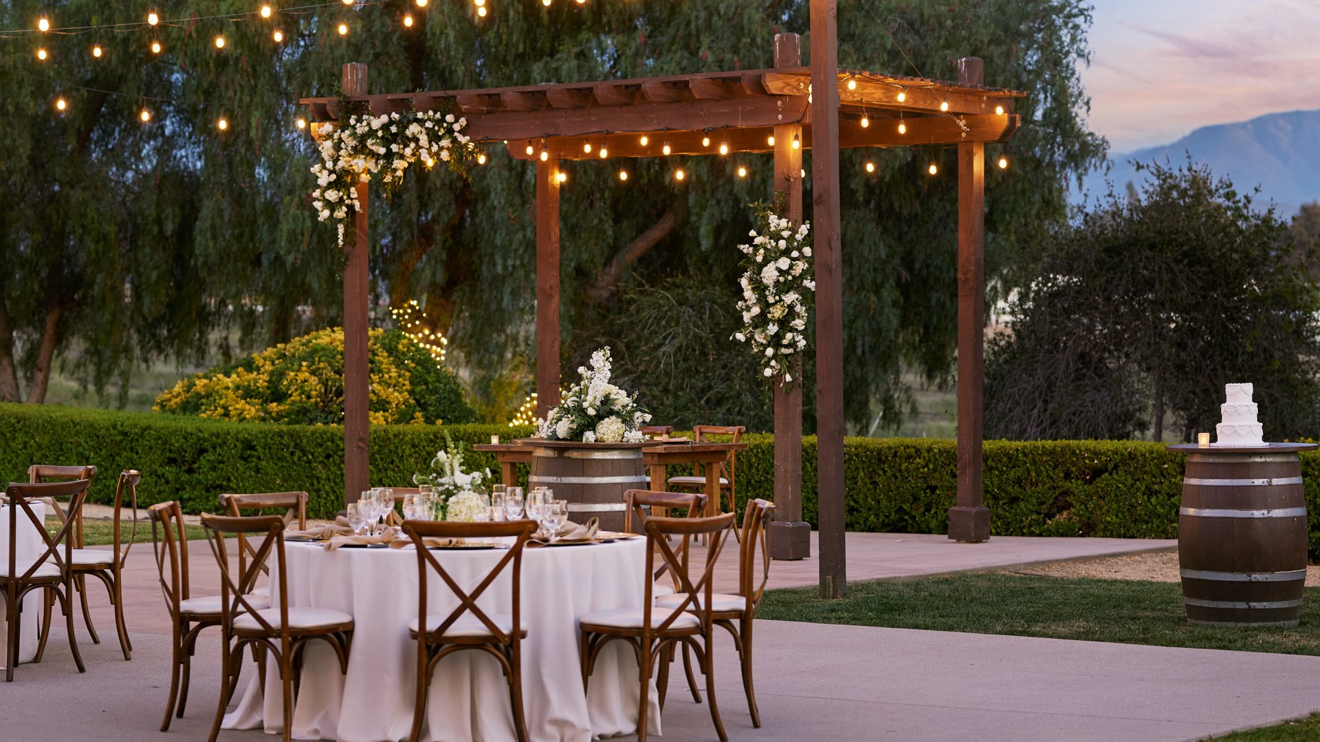 Reception courtyard at Bel Vino Winery featuring pergola draped with florals, string lights, and round guest tables.