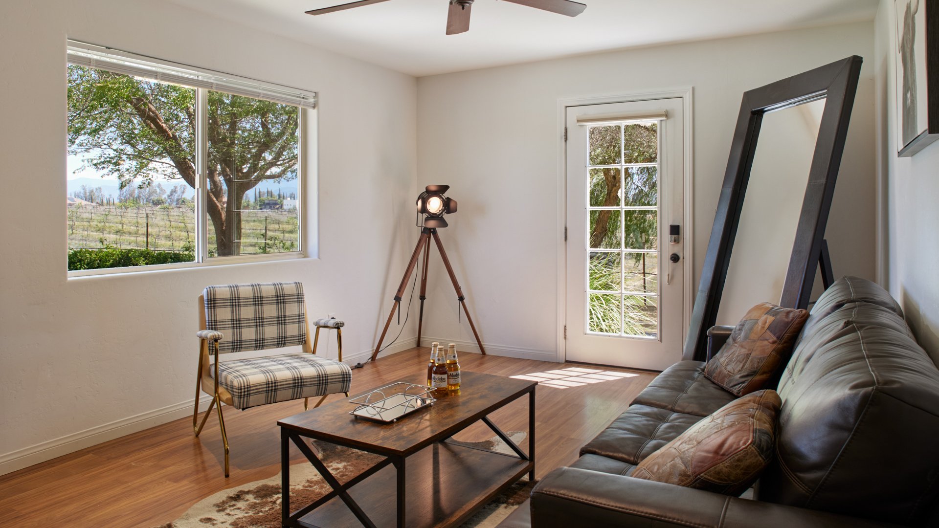 Stylish groom’s suite at Bel Vino Winery with leather sofa, plaid chair, and vineyard view window.