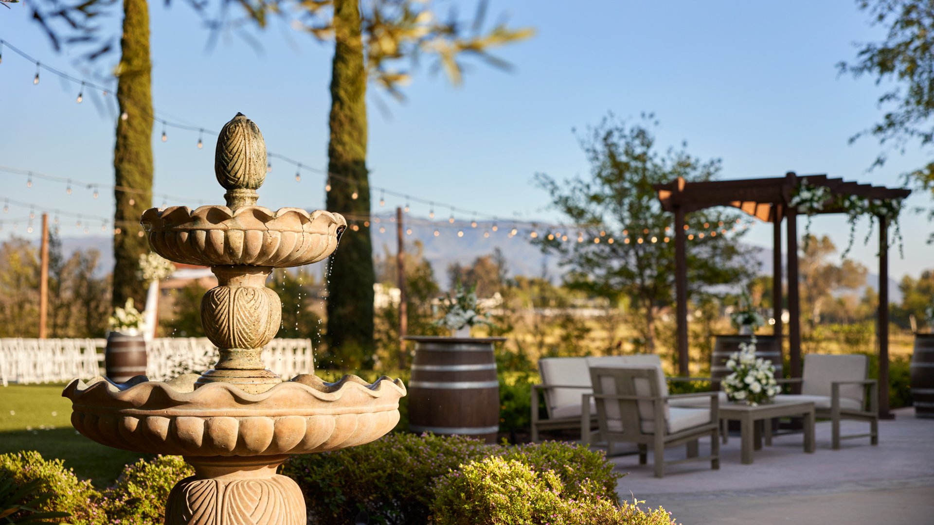 Close-up of stone fountain on the cocktail patio at Bel Vino Winery with lounge seating and vineyard ceremony space in view.