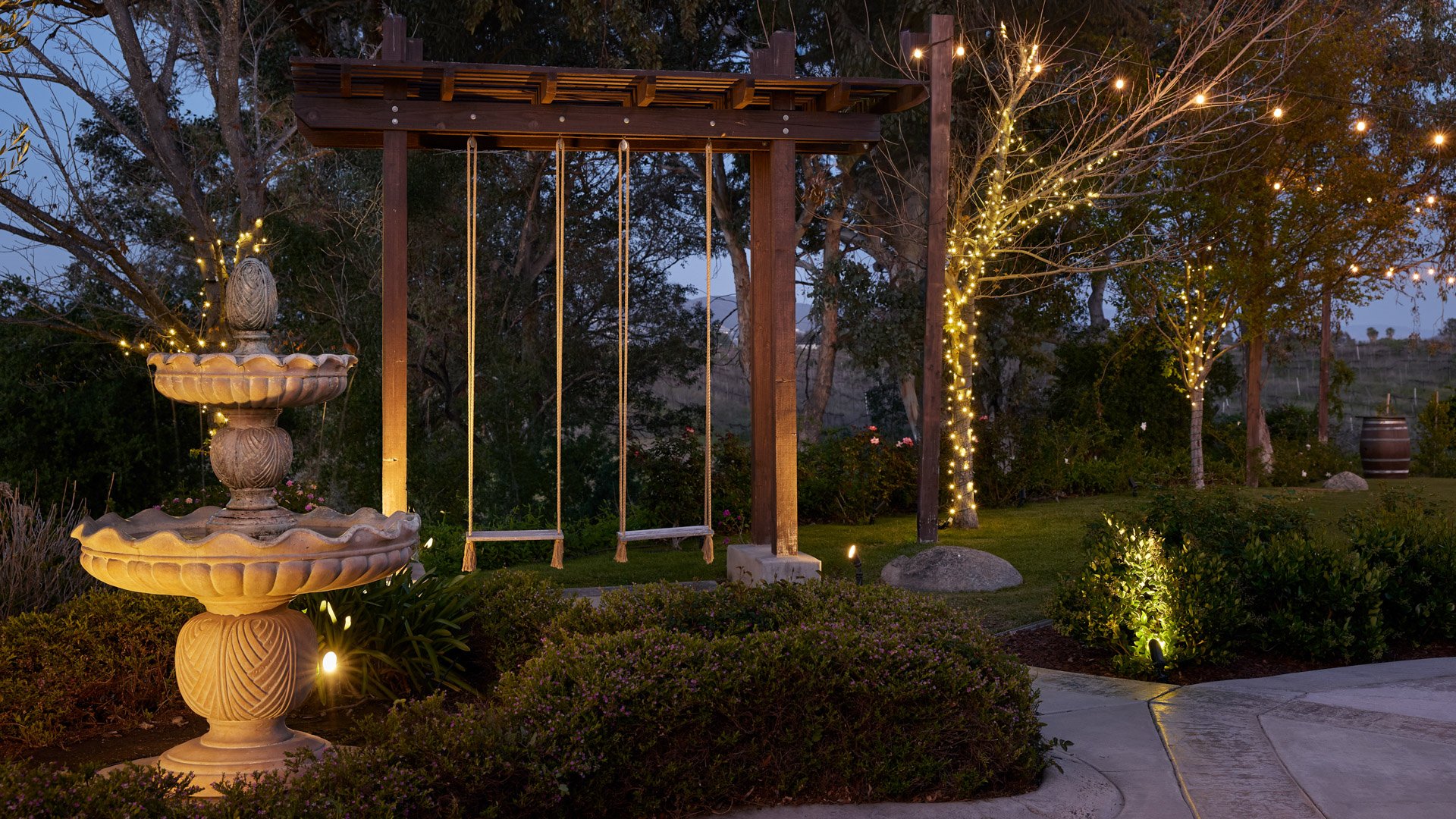 Stone fountain and swing illuminated with string lights at Bel Vino Winery cocktail patio during an evening wedding.