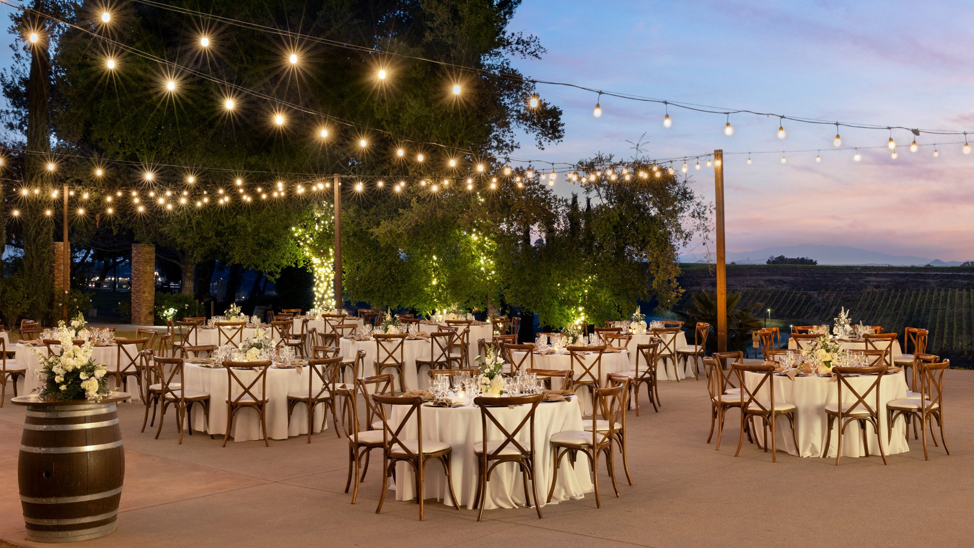 Courtyard wedding reception at Bel Vino Winery with glowing string lights, elegant tables, and vineyard views at dusk.