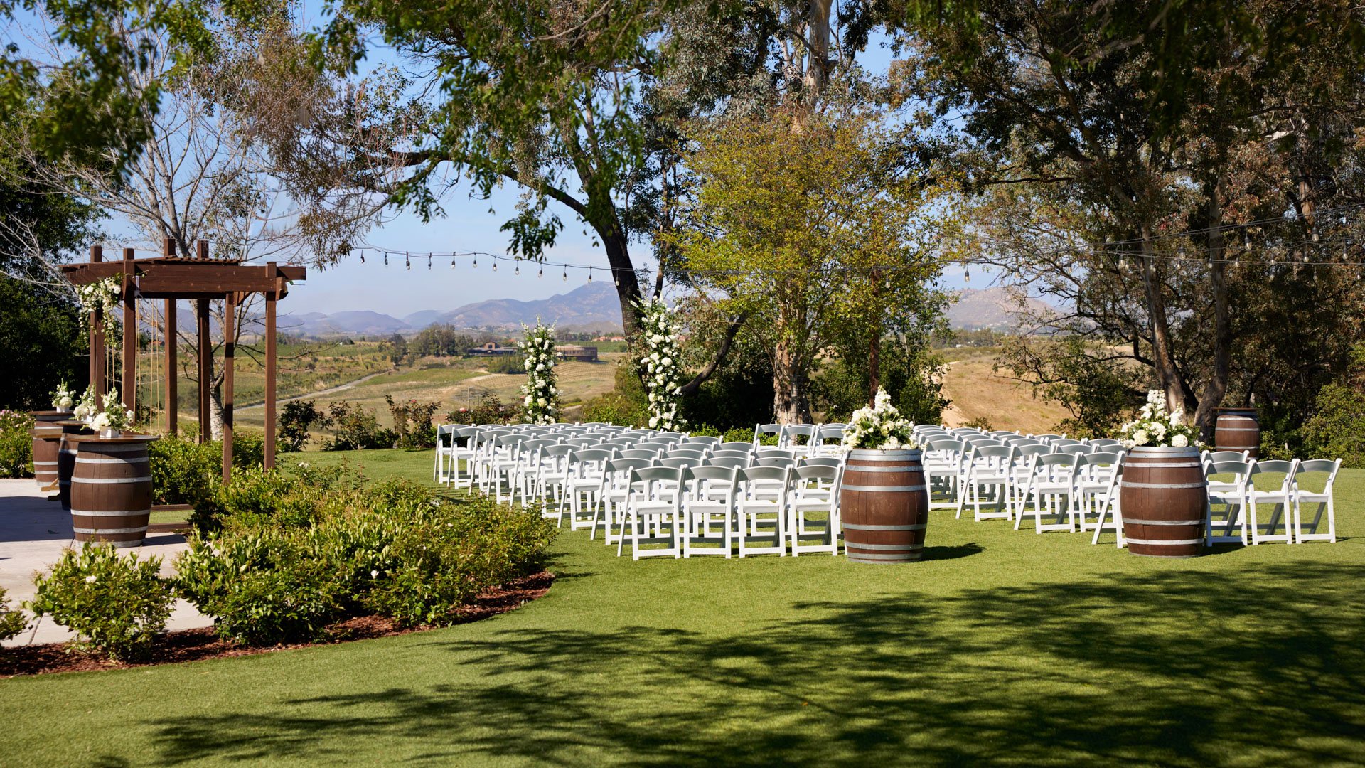 Wedding ceremony lawn at Bel Vino Winery with lush greenery, vineyard views, and classic white ceremony seating.