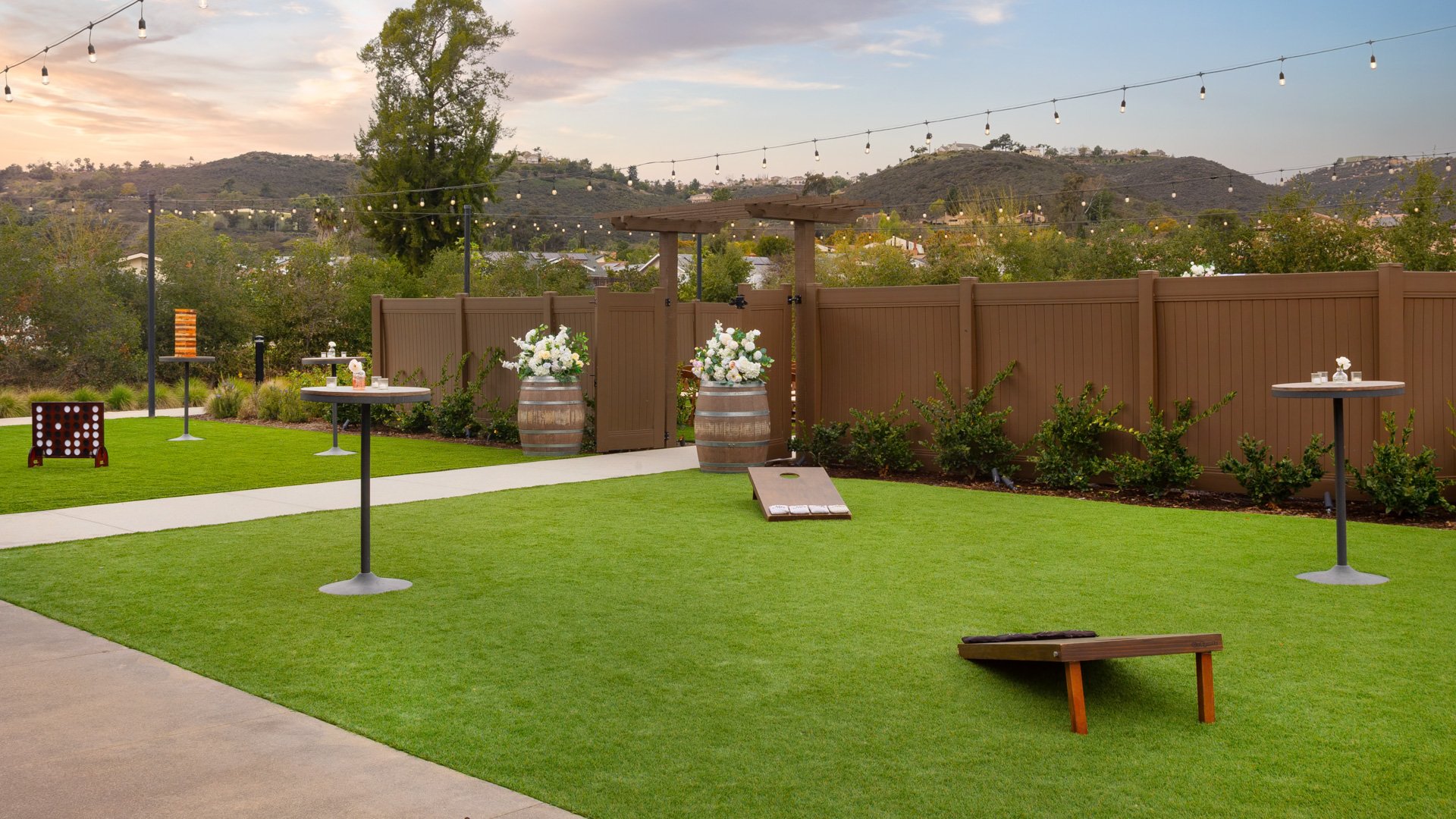 Outdoor cocktail patio with lawn games, high-top tables, and string lights at Canopy Grove wedding venue in Escondido, California.