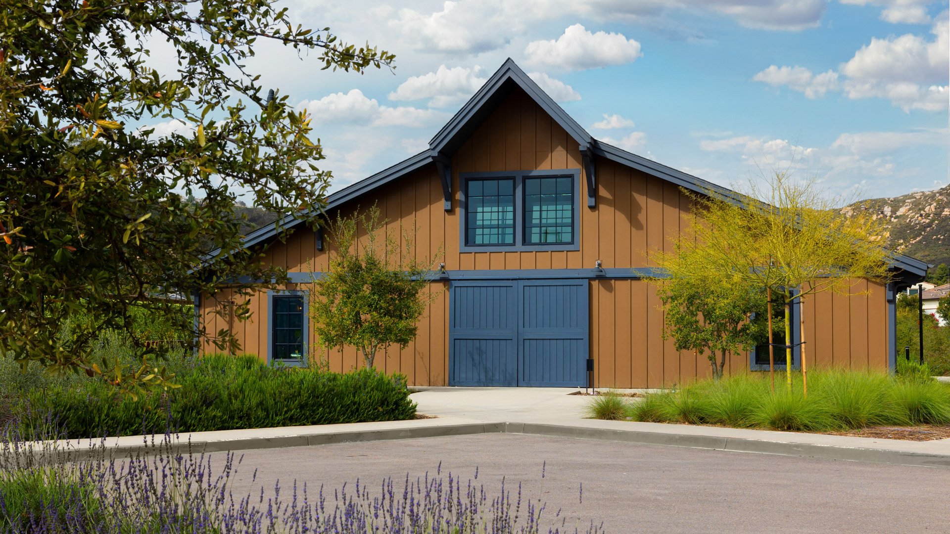 Aerial view of Canopy Grove’s ceremony lawn with wooden chairs arranged around a decorated archway.xterior view of Canopy Grove’s barn with brown siding, blue trim, and surrounding natural landscaping in Escondido, CA.