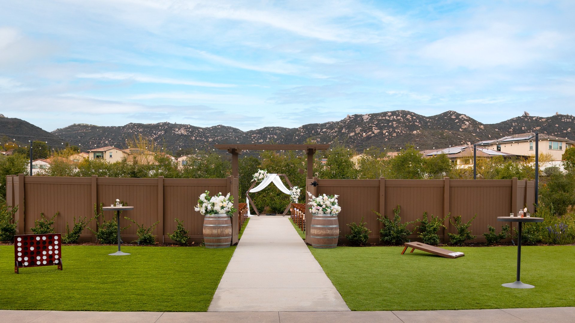 Outdoor ceremony lawn entrance at Canopy Grove featuring floral arrangements on wine barrels, pergola, and mountain views.