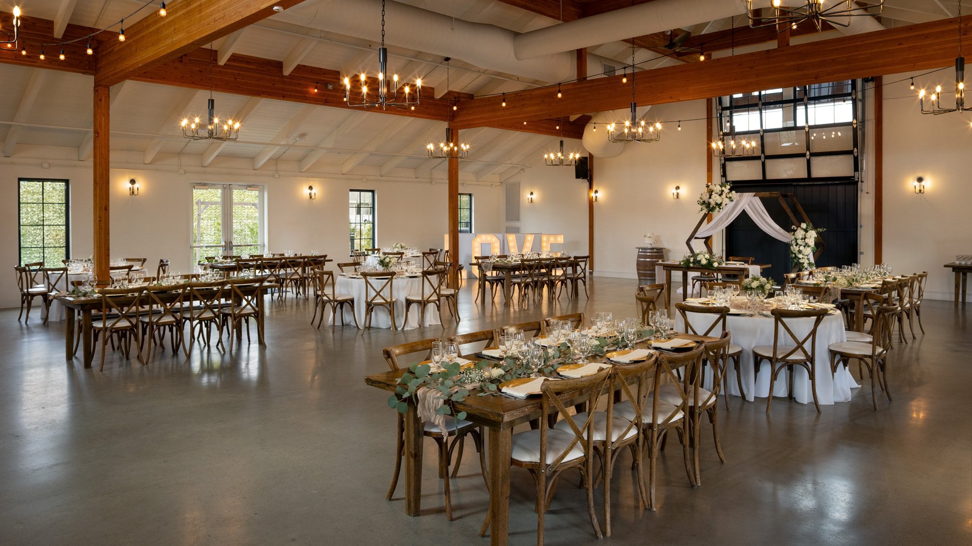 Elegant barn wedding reception with wood tables, greenery centerpieces, and glowing chandeliers at Canopy Grove in Escondido, CA.