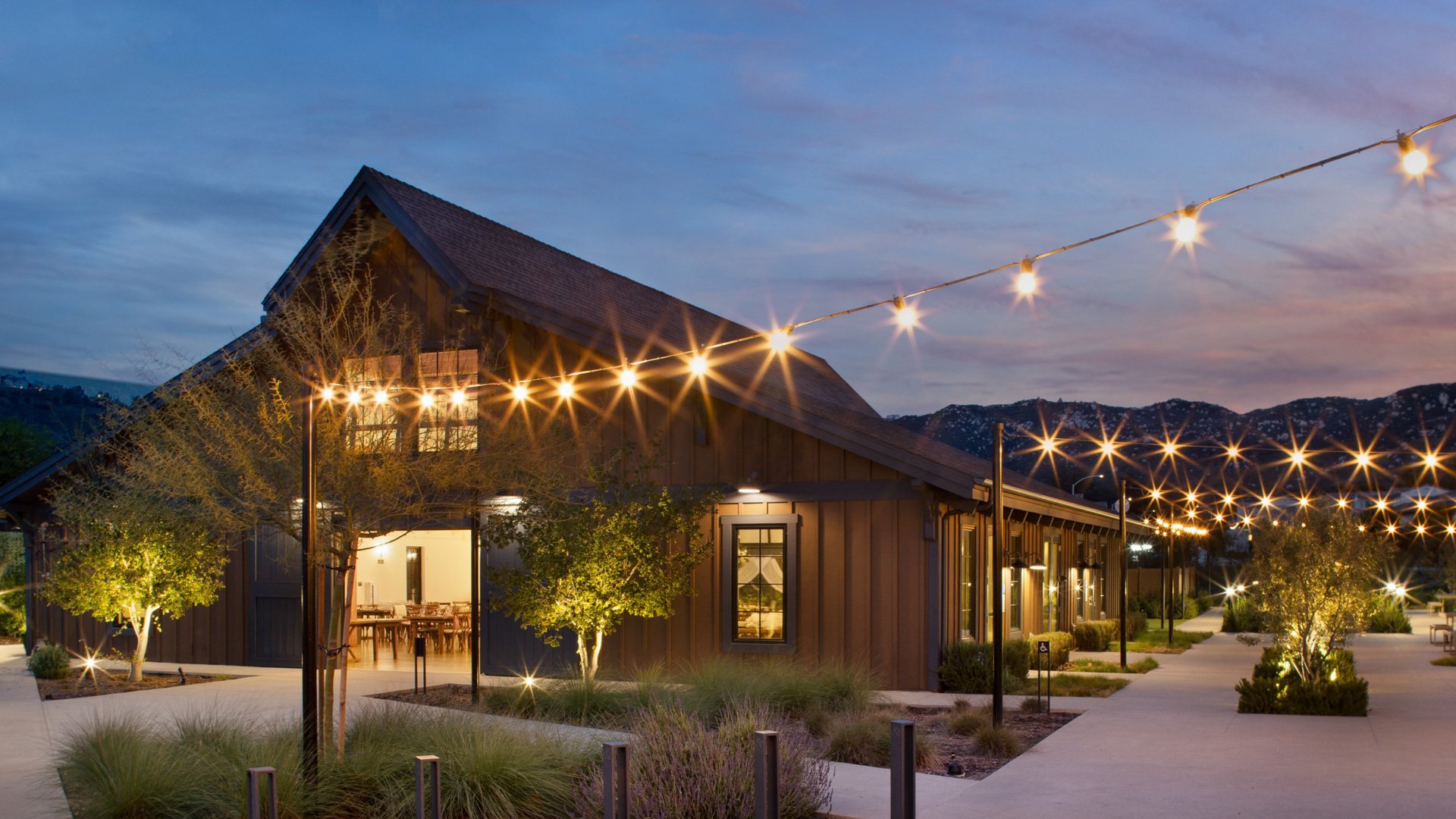 Evening view of Canopy Grove wedding barn illuminated with glowing string lights and surrounded by landscaped walkways.