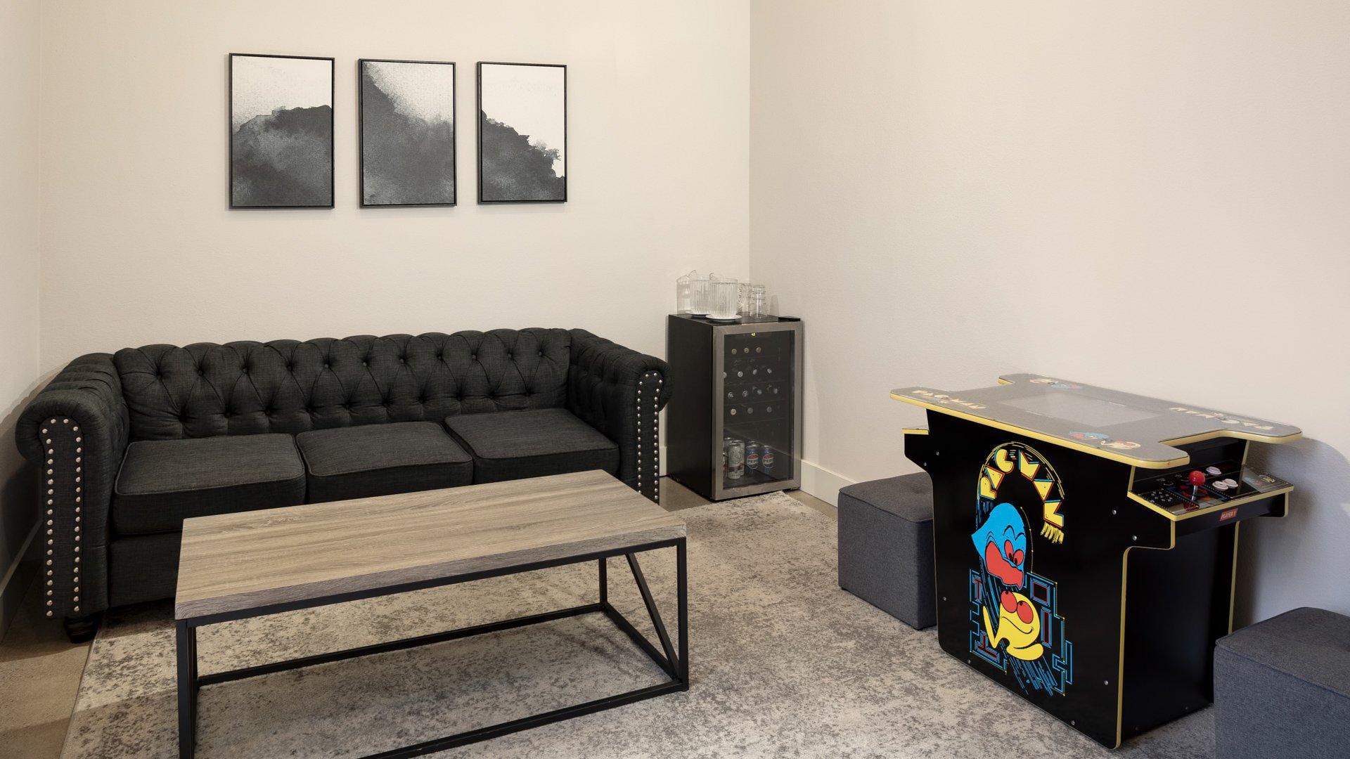 Modern groom’s lounge featuring a black sofa, arcade game, mini fridge, and rustic coffee table at Canopy Grove wedding venue.