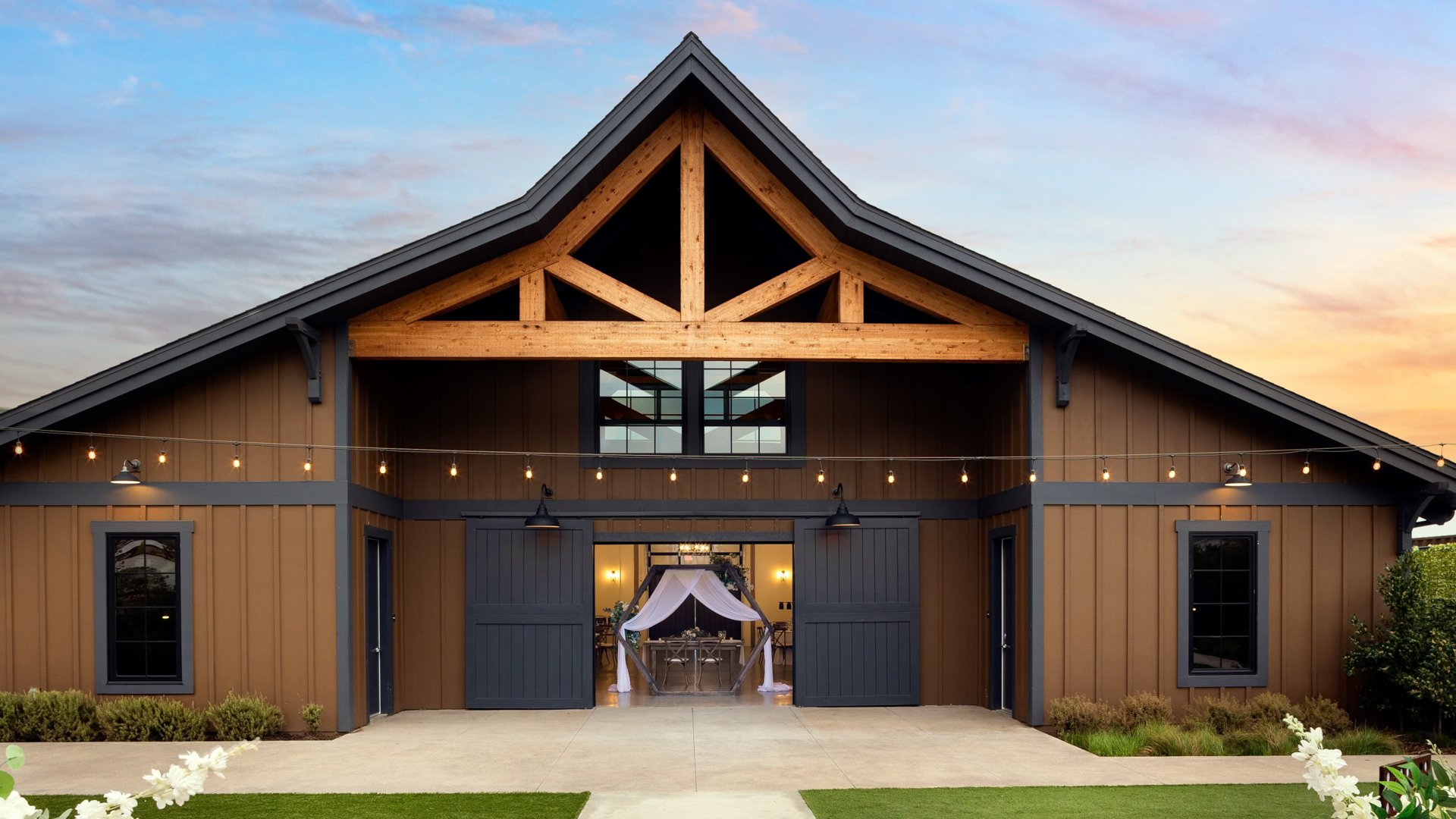 Exterior view of Canopy Grove’s rustic barn with string lights and open barn doors revealing wedding décor inside.