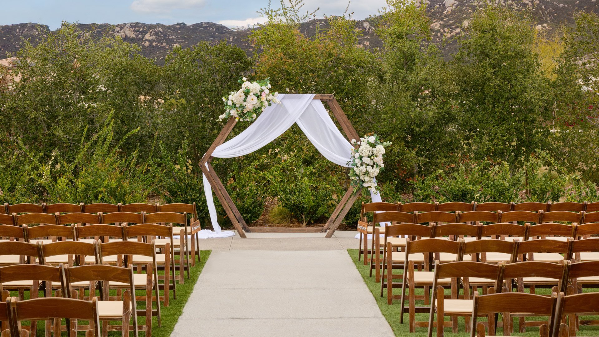 Wooden hexagon arch draped with white fabric and adorned with floral arrangements at Canopy Grove’s outdoor ceremony lawn.