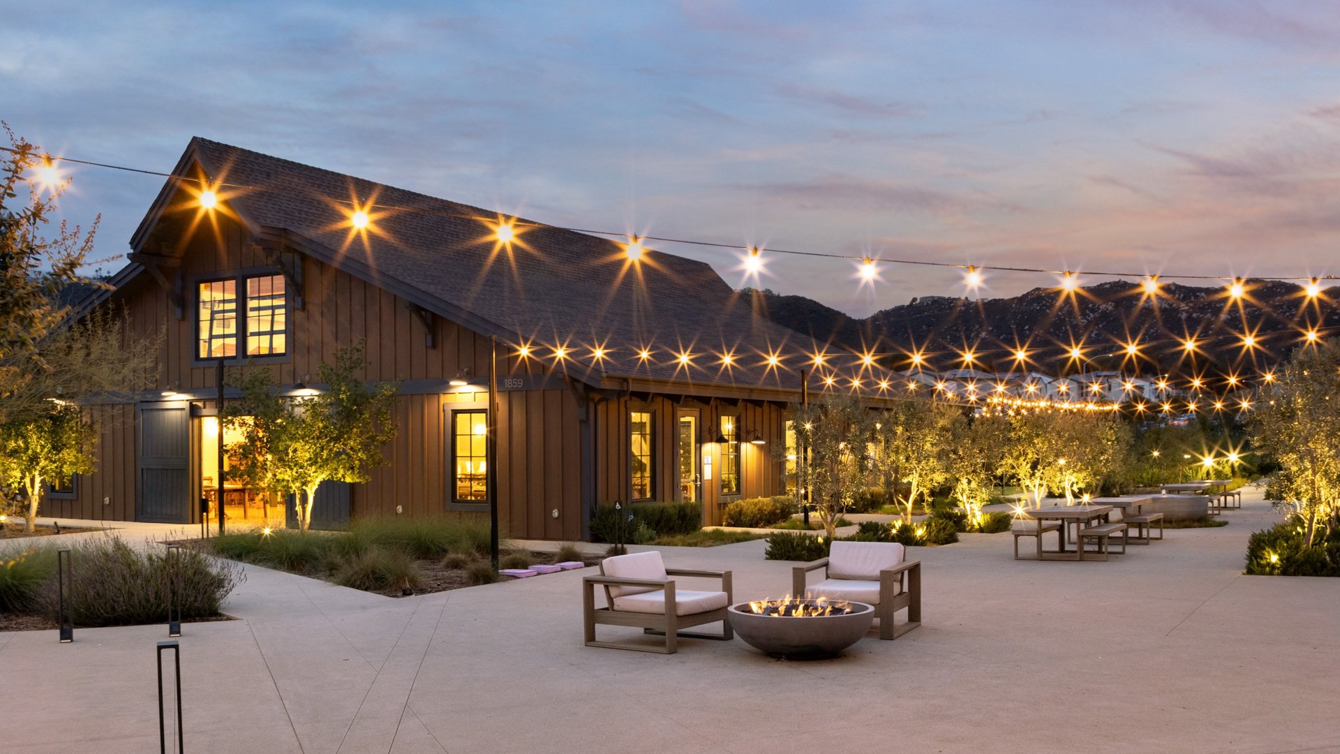 Twilight view of Canopy Grove’s outdoor cocktail patio with cozy seating, firepits, and glowing string lights against mountain views.