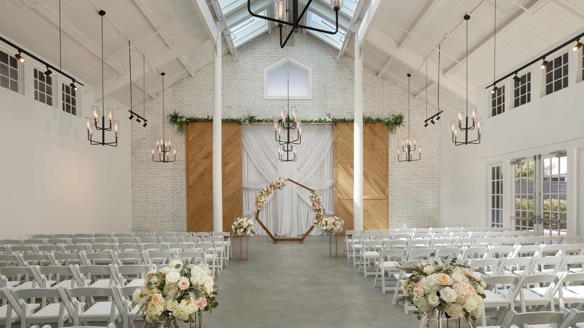 Bright Carlsbad Windmill chapel wedding ceremony with floral hexagon arch and white chairs.