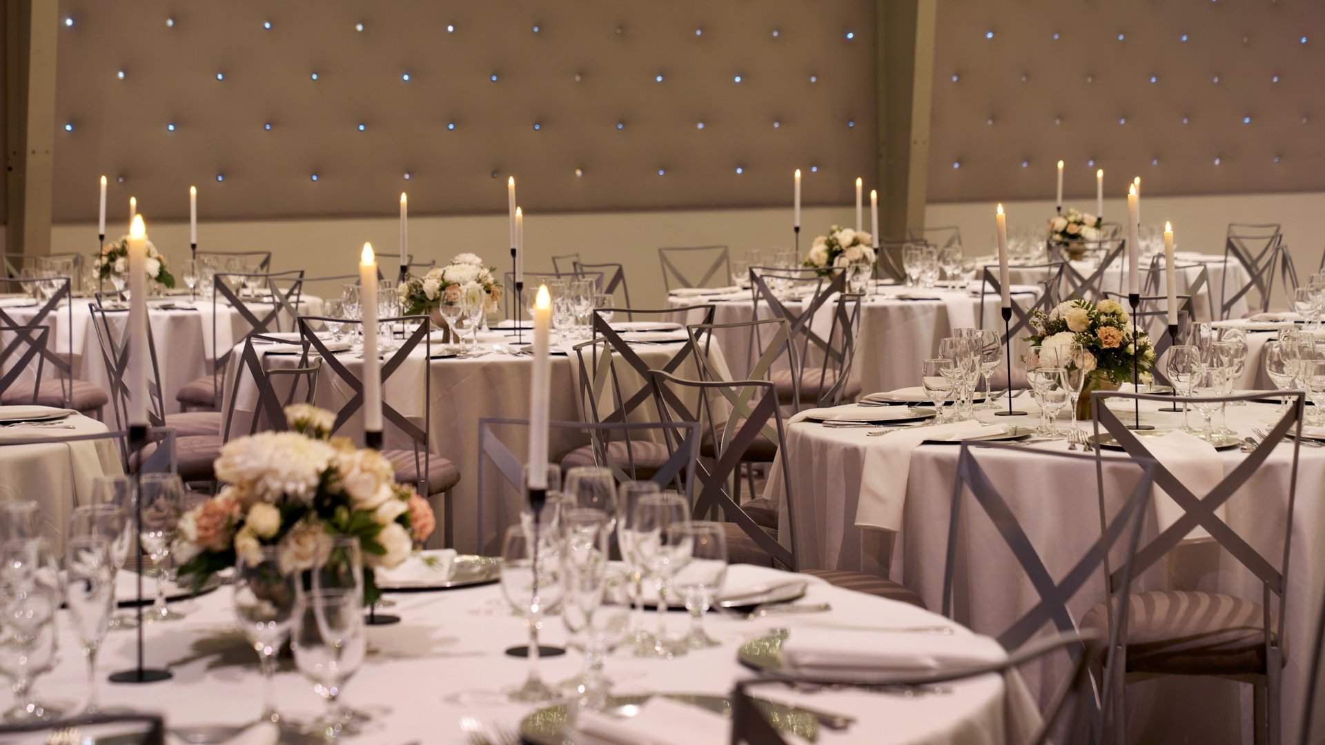 Close-up view of a wedding reception setup at The Clayton House Hangar in Scottsdale, Arizona, featuring candlelit tables with ivory linens, crystal glassware, and soft floral arrangements under twinkling ceiling lights.