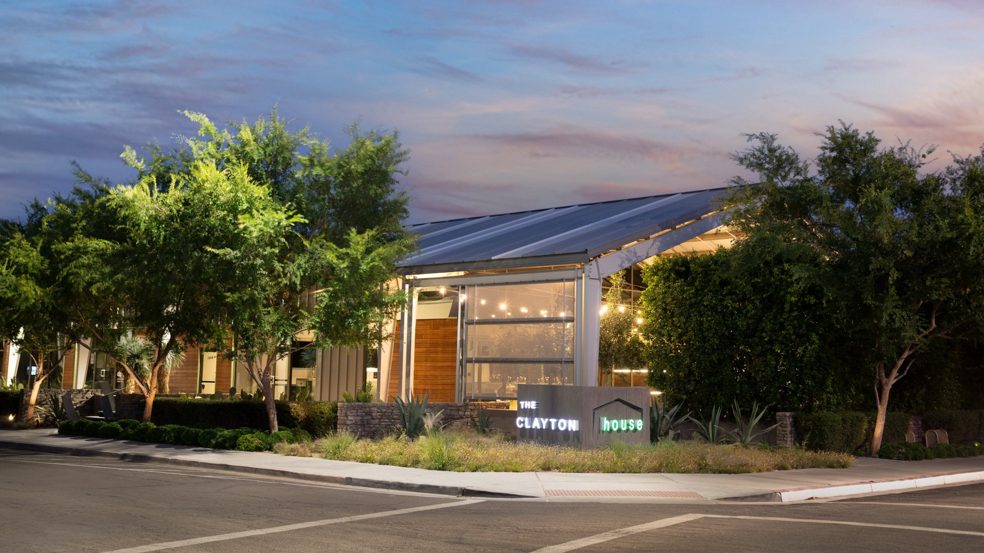 Exterior view of The Clayton House in Scottsdale, Arizona, at twilight with illuminated signage, greenery, and modern architectural design glowing beneath the evening sky.