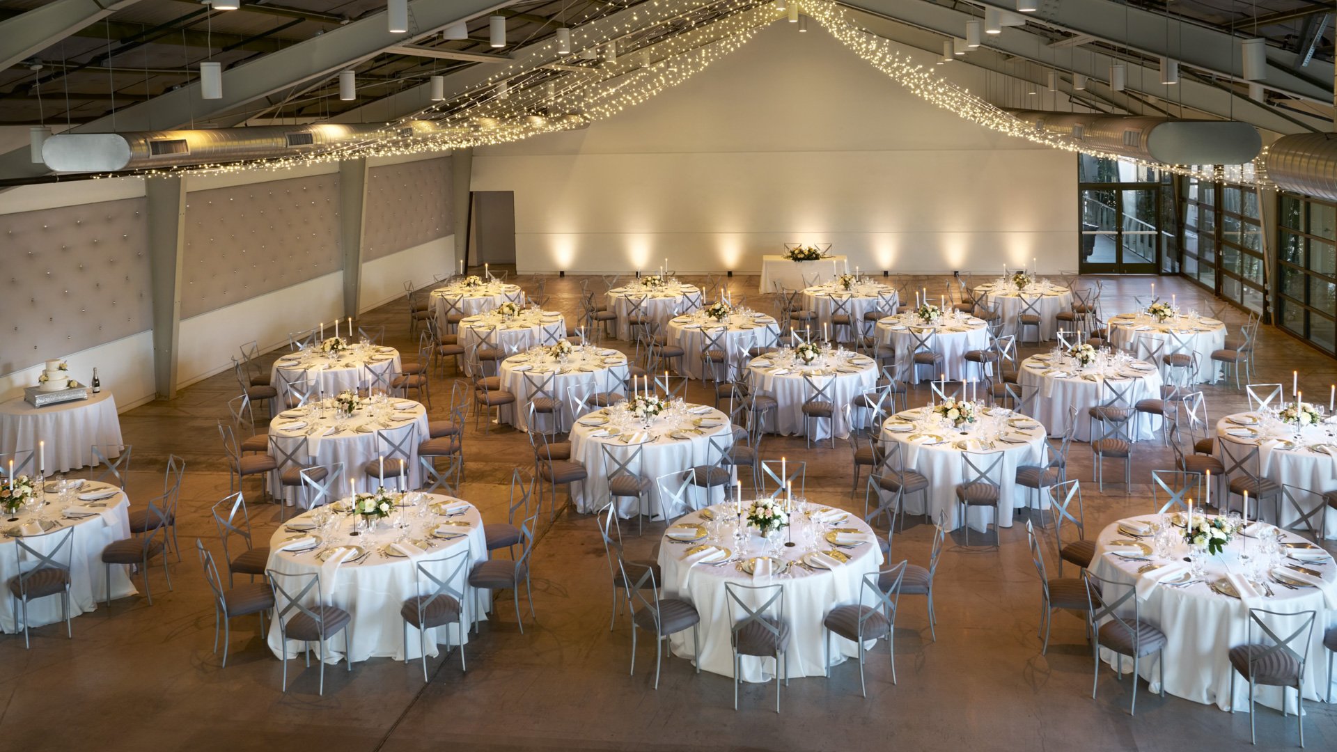 The Hangar at The Clayton House in Scottsdale, Arizona, beautifully arranged for a wedding reception with round tables, white linens, gold accents, and soft string lighting overhead.