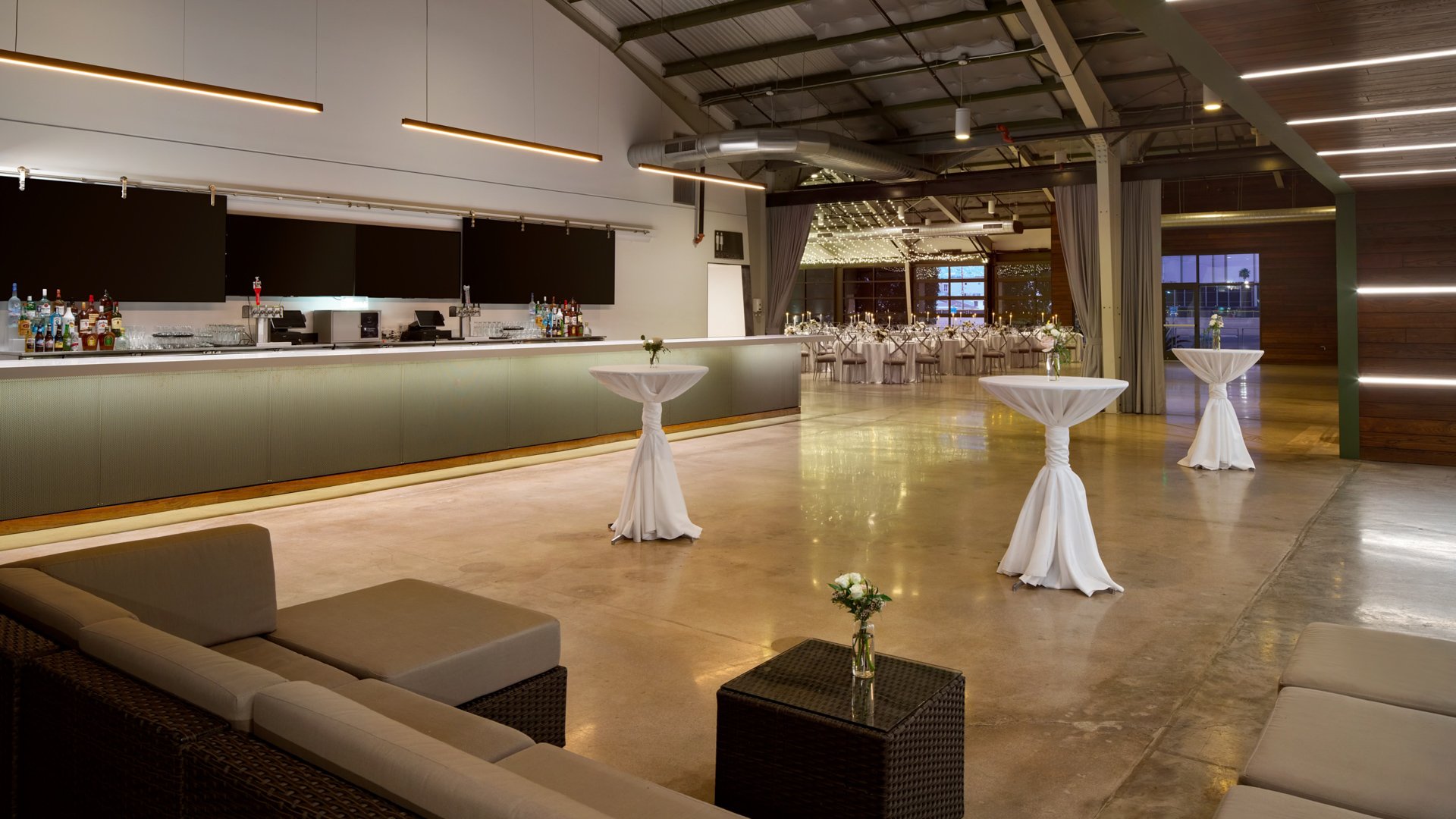 The Clayton House Atrium in Scottsdale, Arizona, styled for cocktail hour with white high-top tables, modern lounge furniture, and warm lighting connecting indoor and outdoor spaces seamlessly.