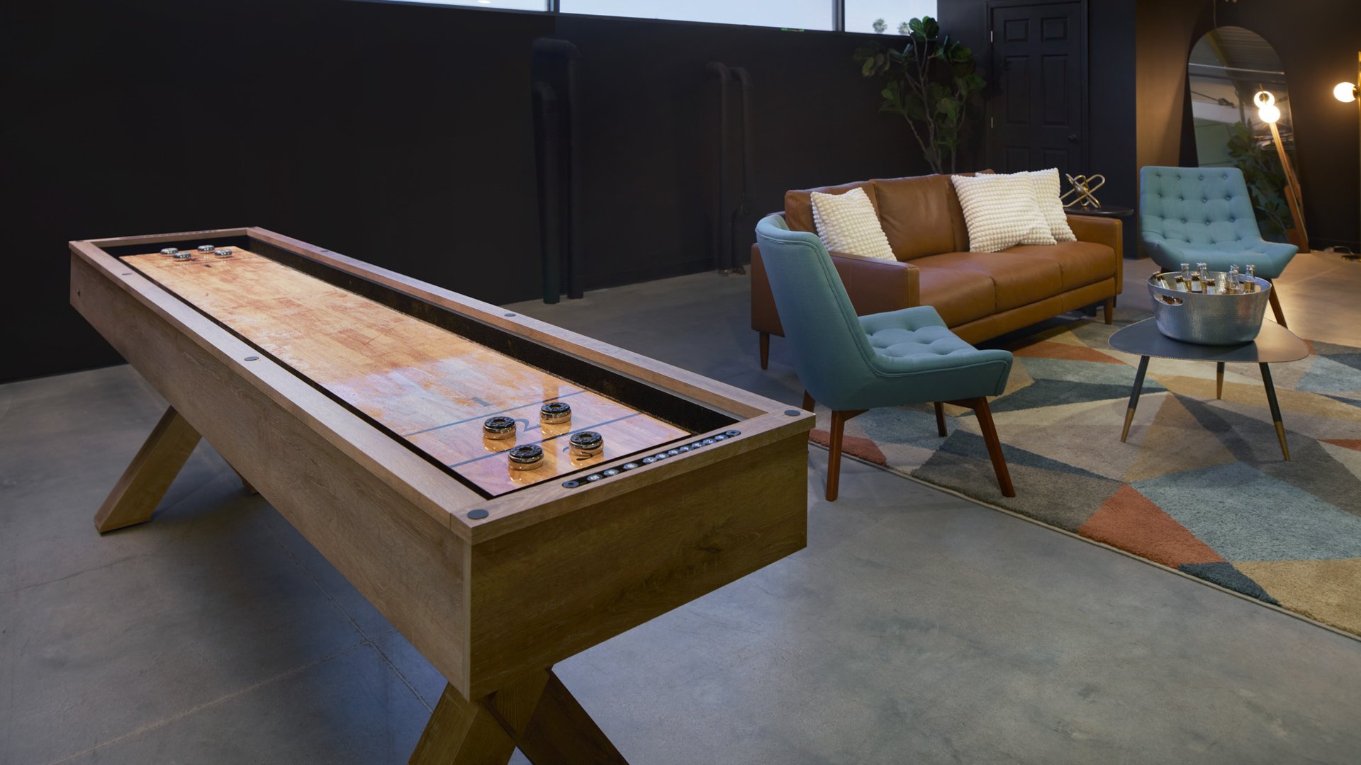 Groom’s lounge at The Clayton House in Scottsdale, AZ, showcasing a shuffleboard table, brown leather sofa, mid-century modern chairs, and a colorful geometric rug creating a stylish, laid-back vibe.