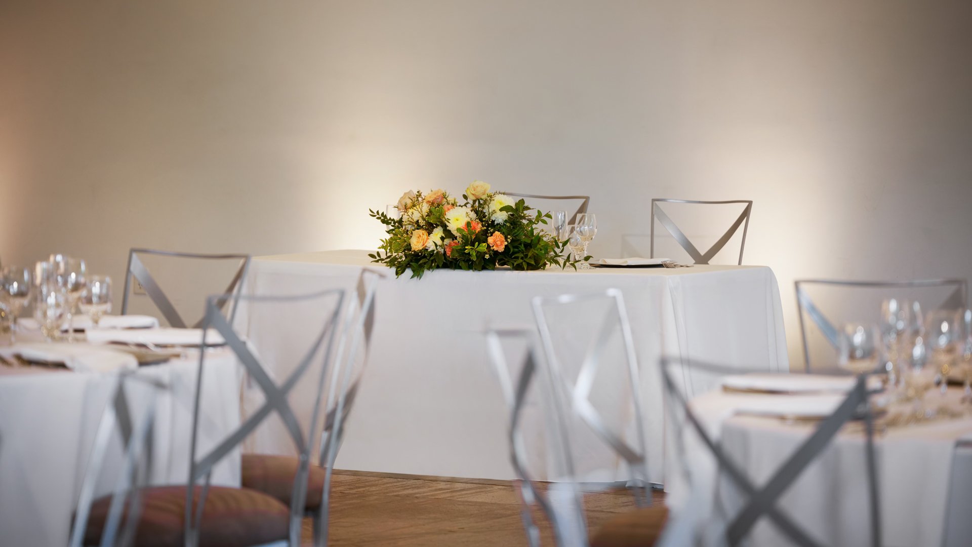 Sweetheart table setup in The Rafters at The Clayton House, Scottsdale, AZ, featuring a white tablecloth, elegant floral centerpiece with peach and cream roses, and soft ambient lighting.