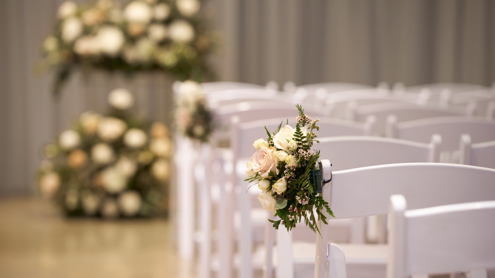 Indoor ceremony setup in The Rafters at The Clayton House, Scottsdale, Arizona, with rows of white chairs and elegant floral aisle arrangements in soft blush and ivory tones.