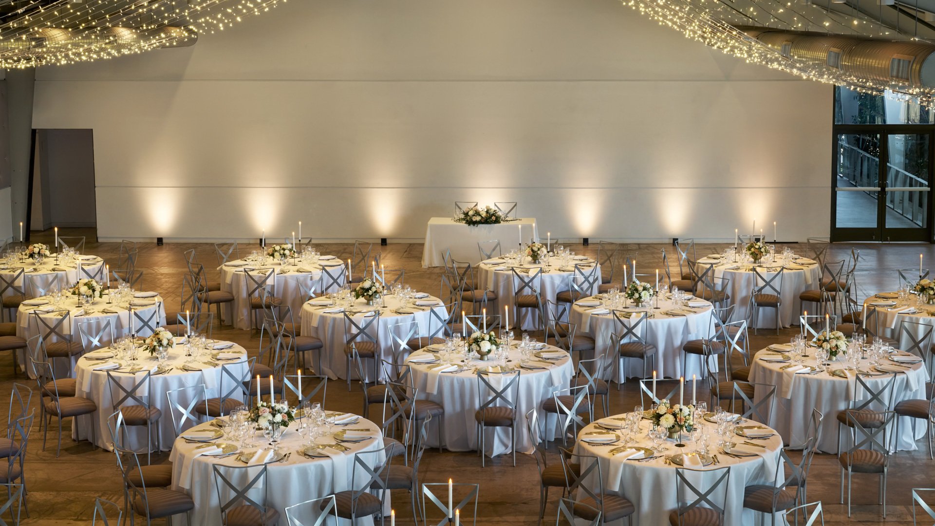 Elegant reception scene inside The Hangar at The Clayton House, Scottsdale, AZ, showcasing round banquet tables, floral centerpieces, tall candles, and sparkling ceiling lights for a sophisticated modern celebration.