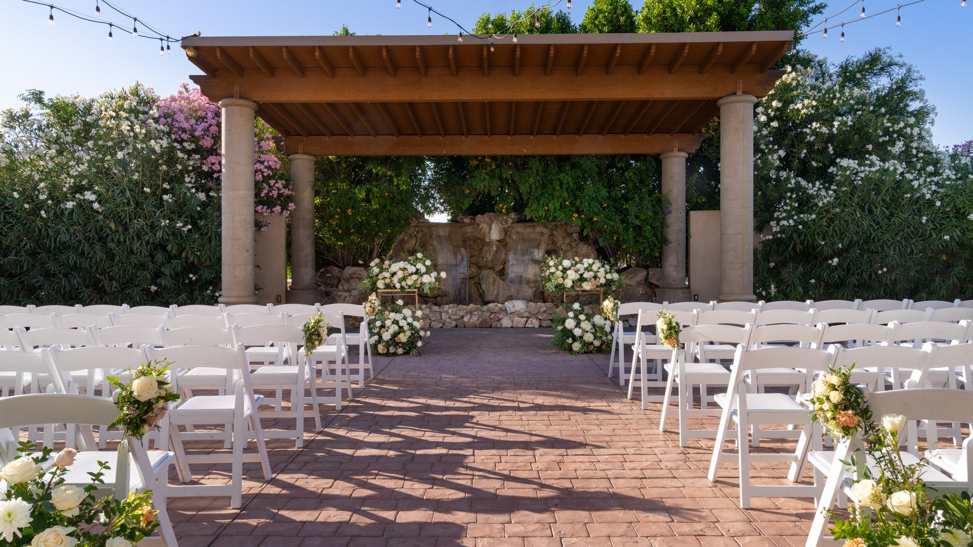 Romantic outdoor wedding ceremony setup at Colby Falls in Arizona featuring a stone waterfall backdrop, white chairs, and floral aisle décor.