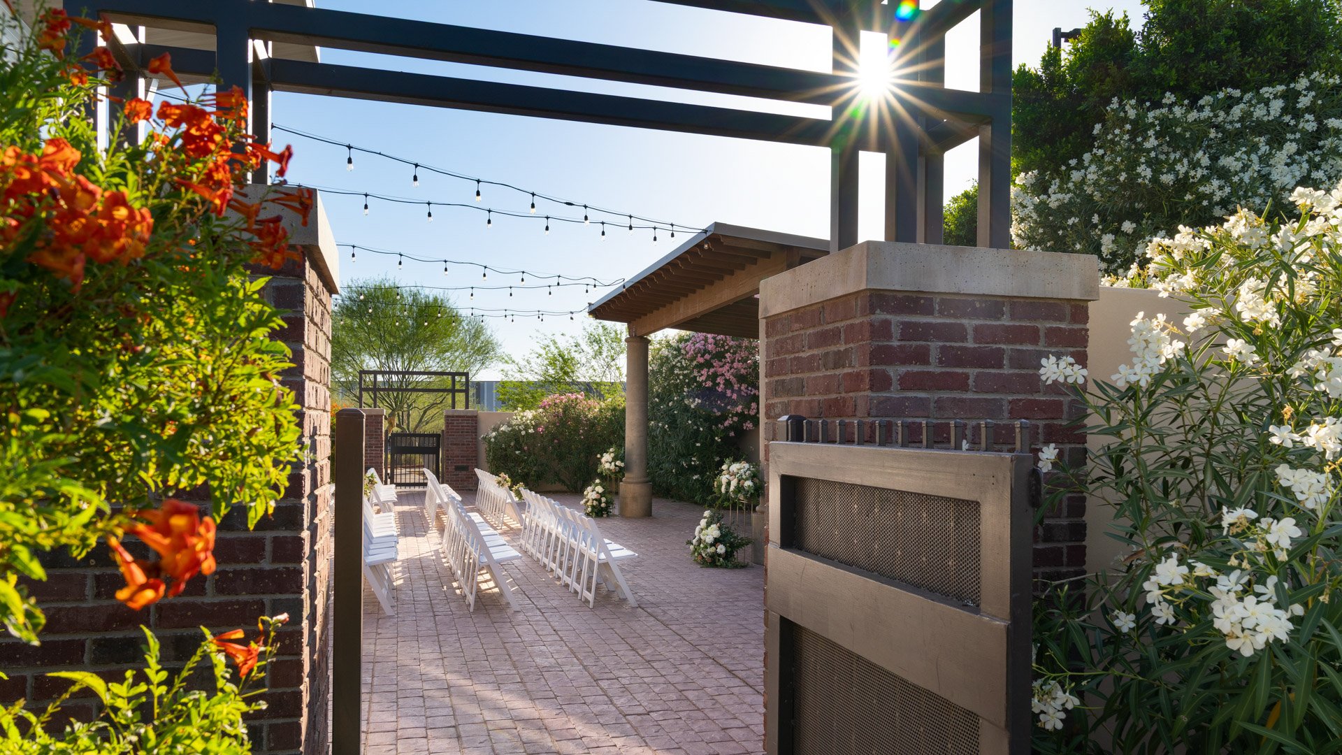 Scenic entrance to the outdoor Grand Waterfall ceremony space at Colby Falls in Arizona with brick pillars, string lights, and floral décor.