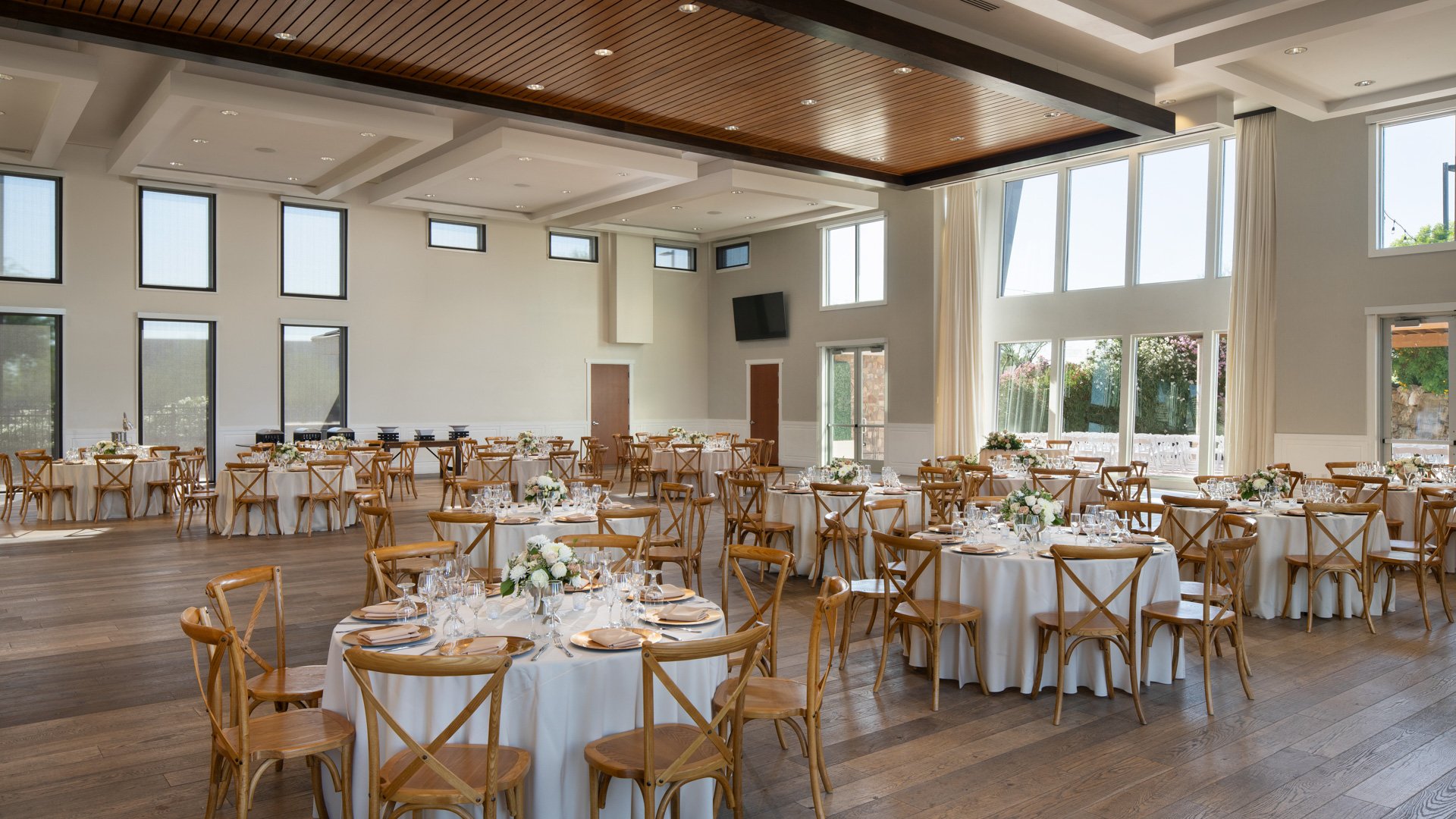 Grand Hall reception at Colby Falls in Arizona with banquet tables, rustic wood chairs, floral centerpieces, and tall windows with natural light.