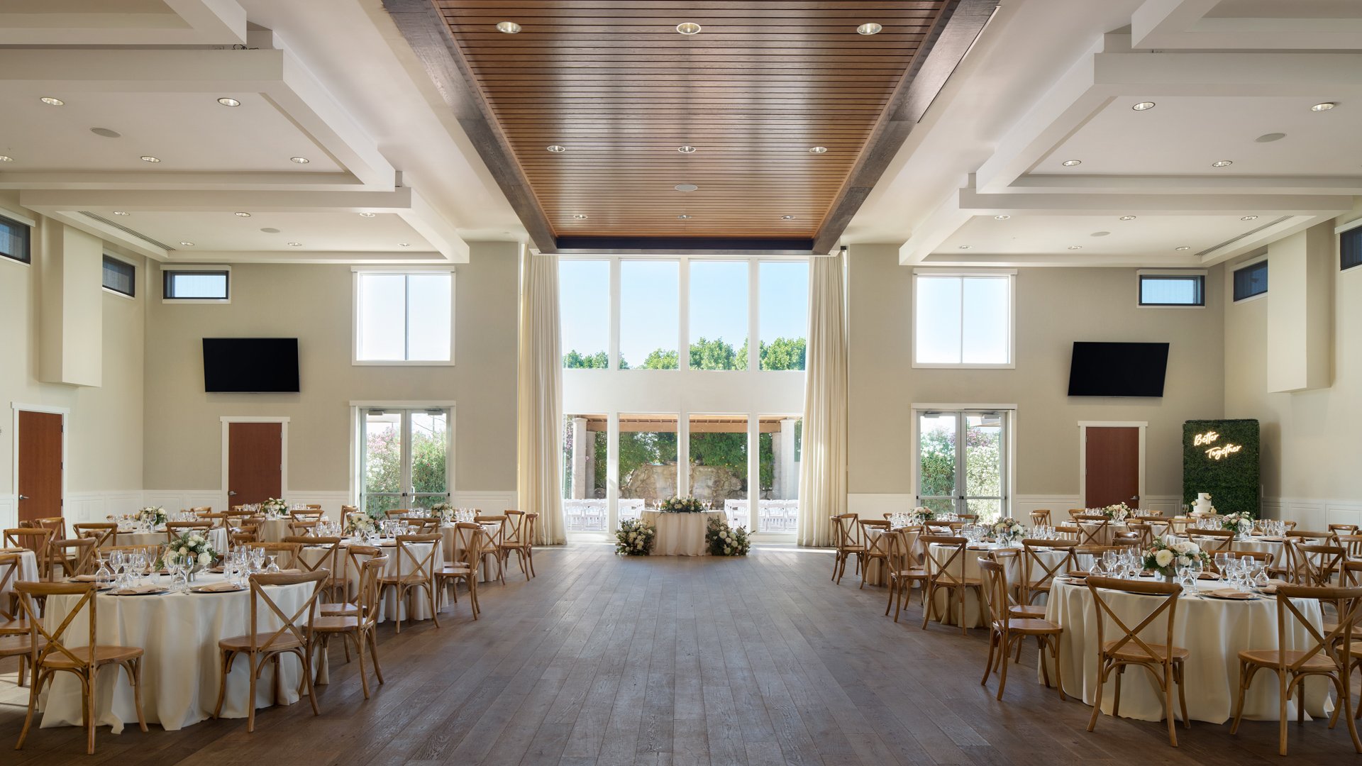 Spacious reception hall at Colby Falls in Arizona with round tables, wood chairs, and large windows overlooking the outdoor ceremony space.