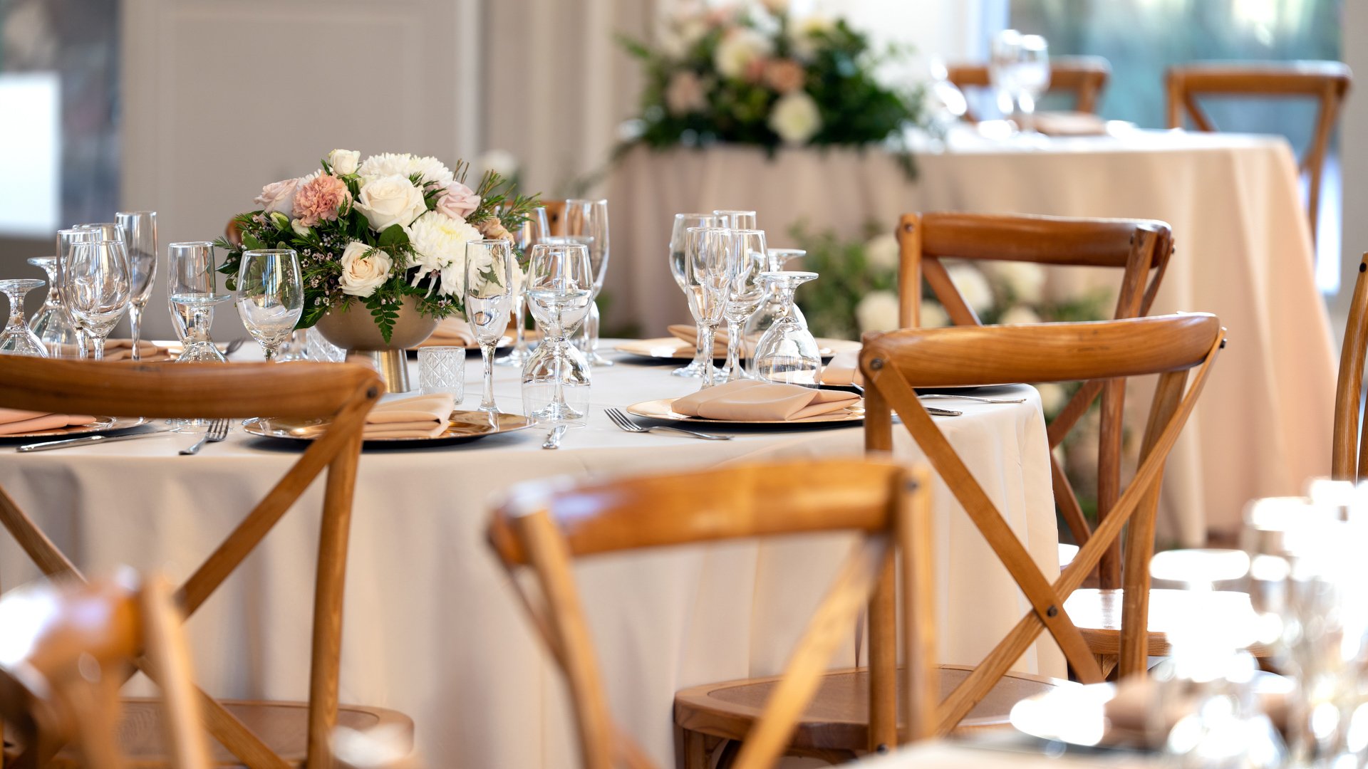 Wedding reception at Colby Falls Grand Hall in Arizona featuring round tables with floral centerpieces, glassware, and wooden cross-back chairs.