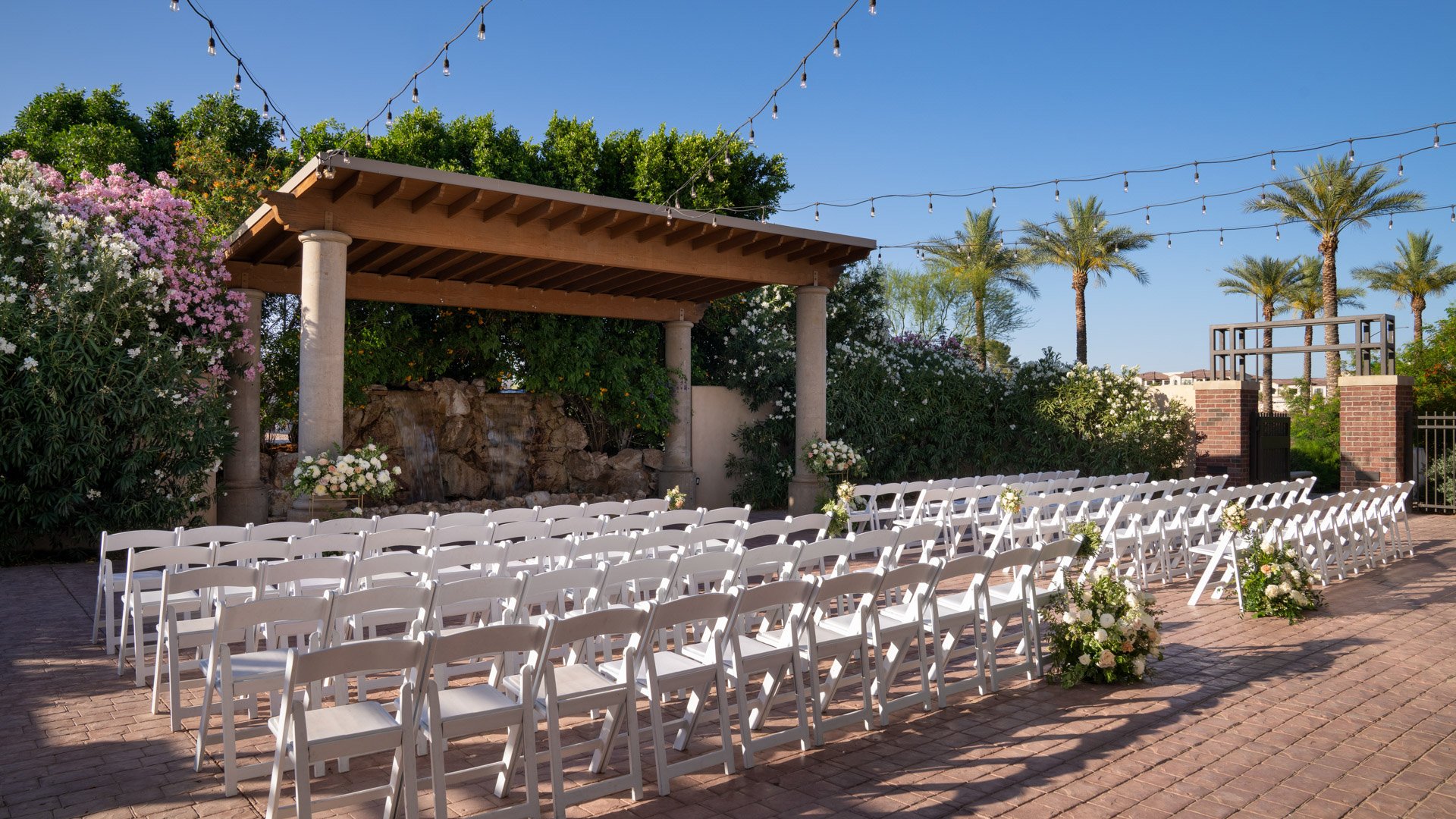 Scenic outdoor ceremony site at Colby Falls Arizona with waterfall backdrop, floral aisle arrangements, and white seating under string lights.