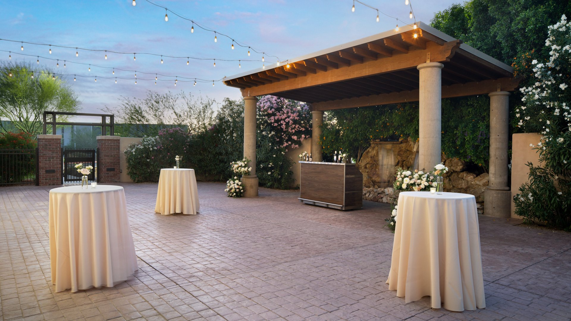 Cocktail hour setup at Colby Falls Waterfall Courtyard in Arizona with high-top tables, string lights, and natural stone waterfall backdrop.