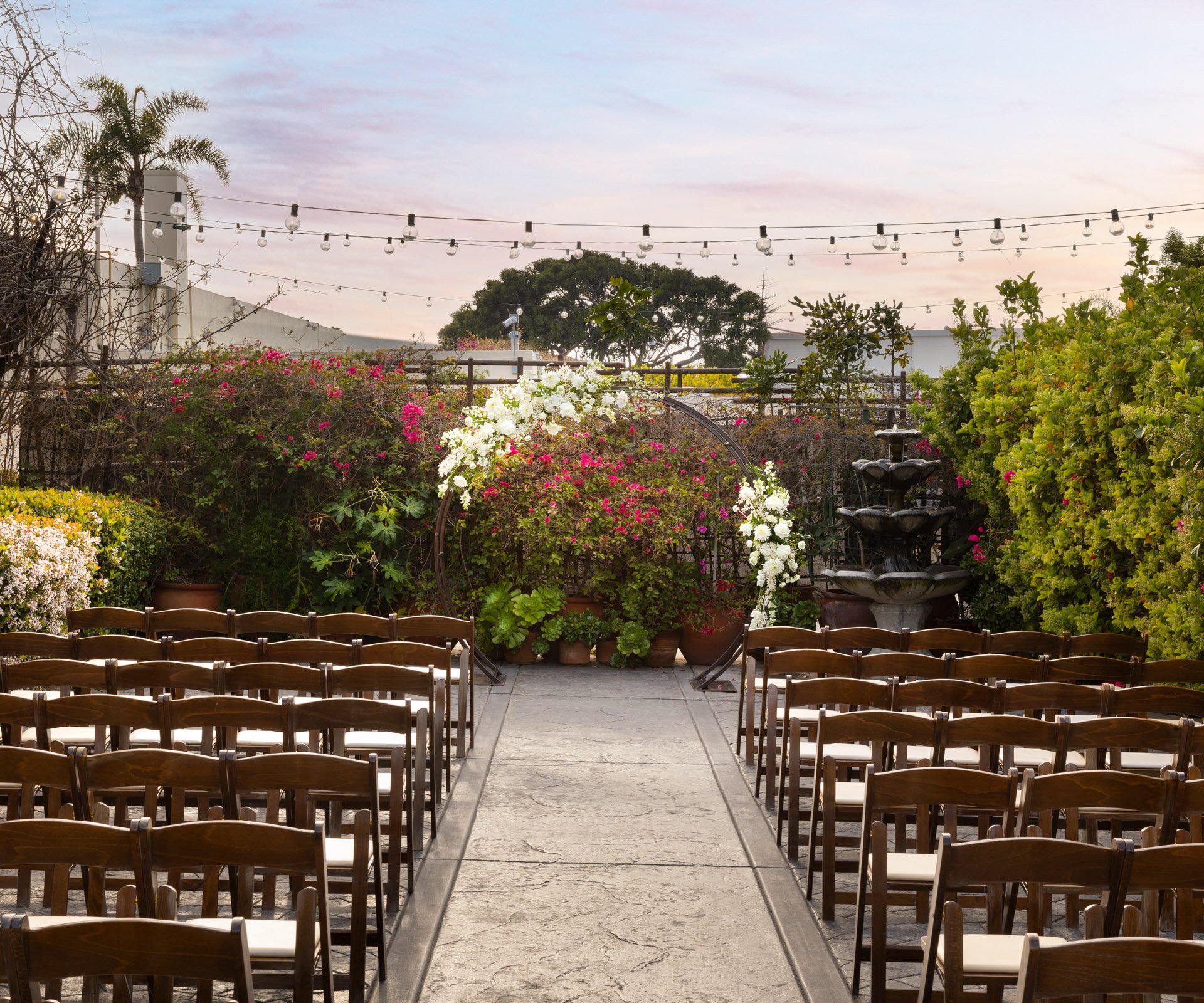 Scenic outdoor garden ceremony with circular arch and stone fountain.