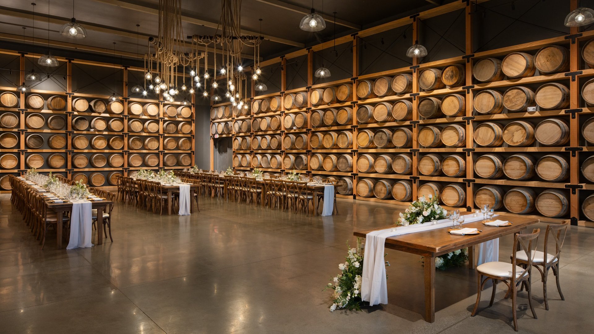 Rustic wedding reception inside the Barrel Room at Danza del Sol Winery in Temecula, CA, featuring wine barrels, long tables, and sweetheart table with floral décor.