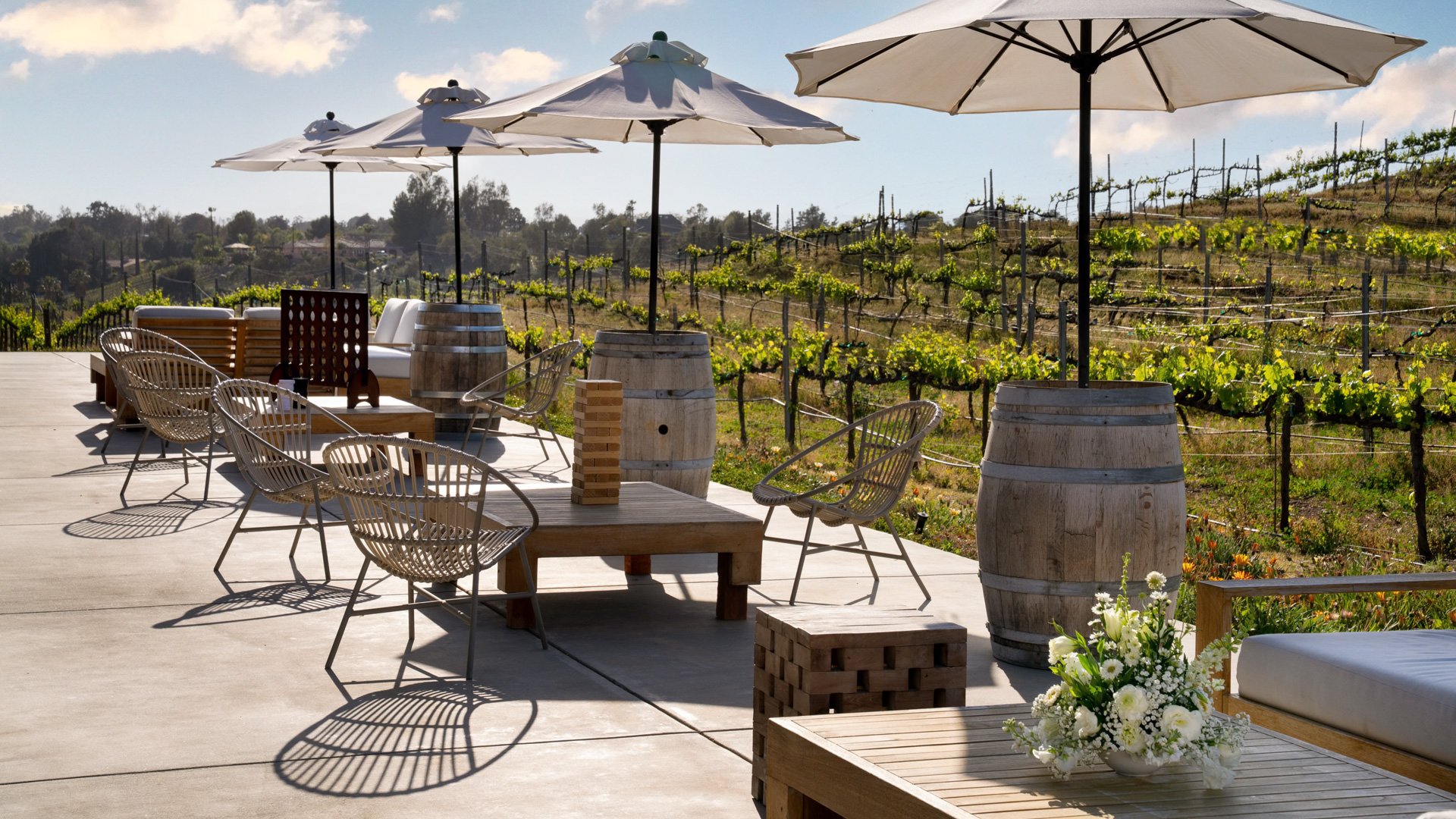 Outdoor cocktail hour space at Danza del Sol Winery in Temecula, CA, with vineyard views, lounge seating, wine barrels, and oversized patio games.