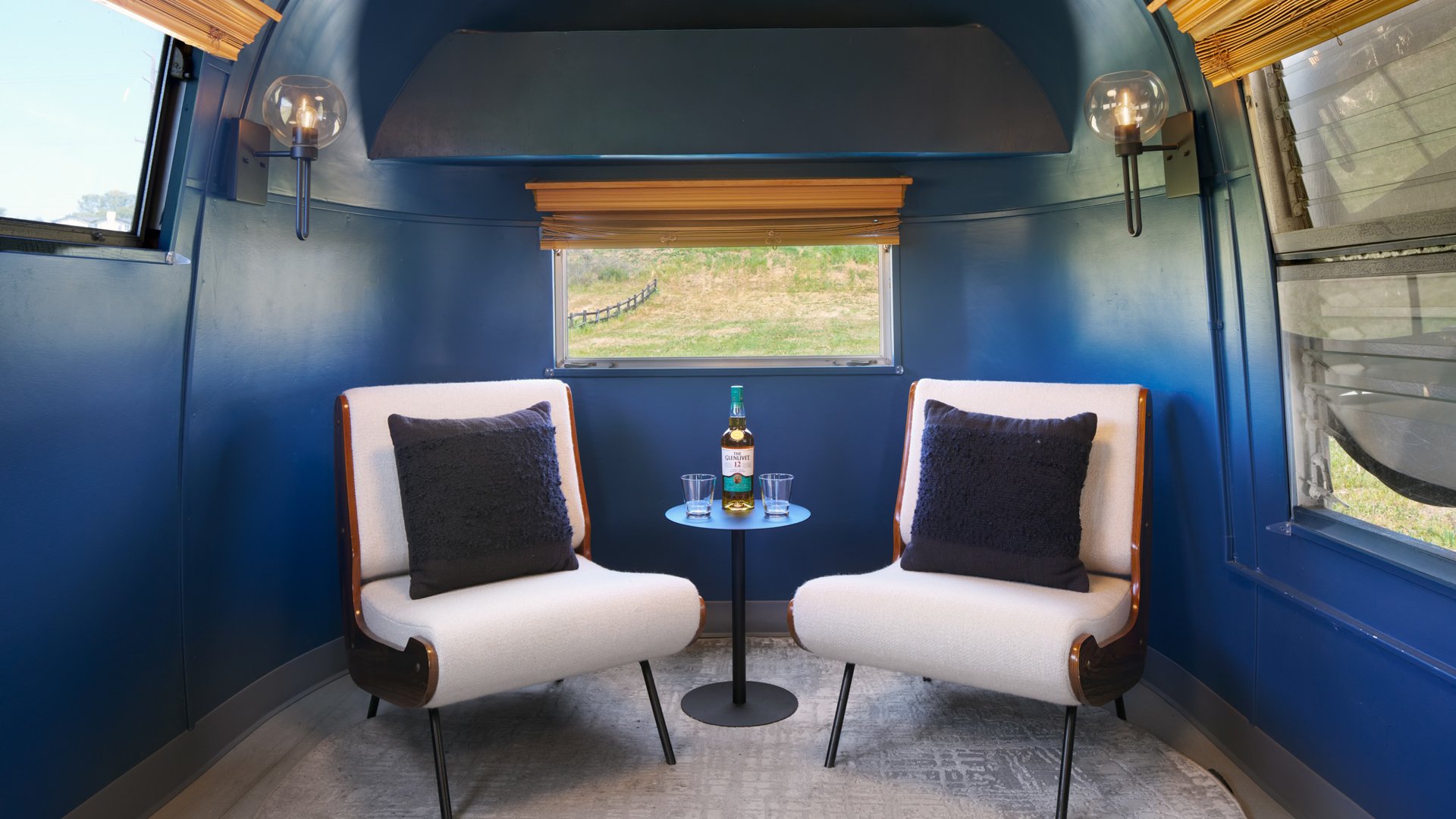 Interior of Silver Airstream Suite at Danza del Sol Winery in Temecula, CA, with cozy seating area, whiskey bottle, and modern blue design.
