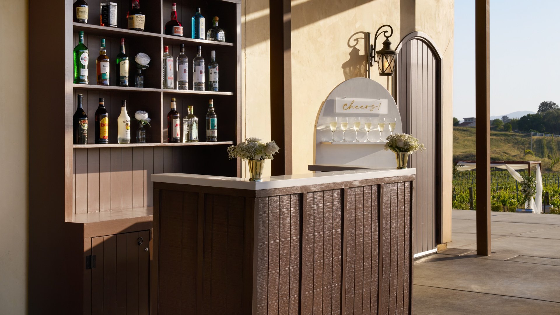 Rustic outdoor wedding bar at Danza del Sol Winery in Temecula, CA, with liquor display shelves, cocktail counter, and vineyard views.