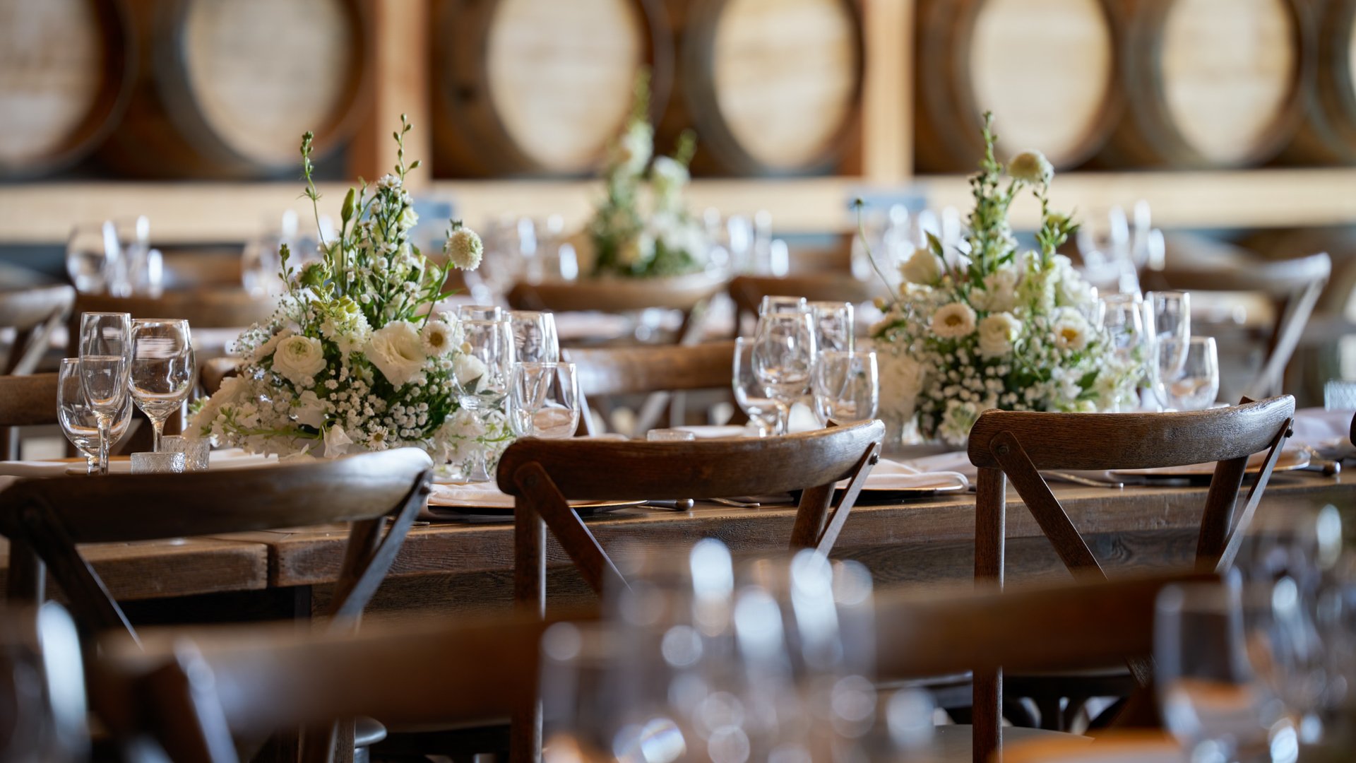 Elegant floral centerpiece with white roses and greenery on a rustic wedding table in the Barrel Room at Danza del Sol Winery, Temecula, CA.