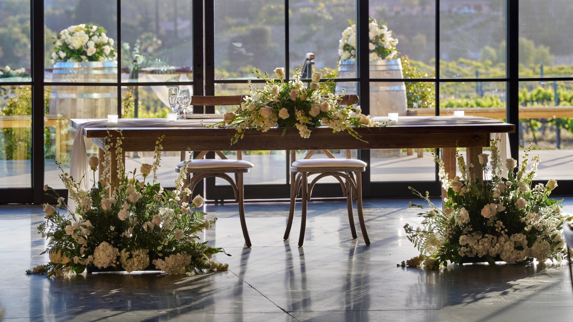 Winery wedding reception at Danza del Sol Winery in Temecula, CA, with wine barrel walls, long banquet tables, and sweetheart table decorated with florals.