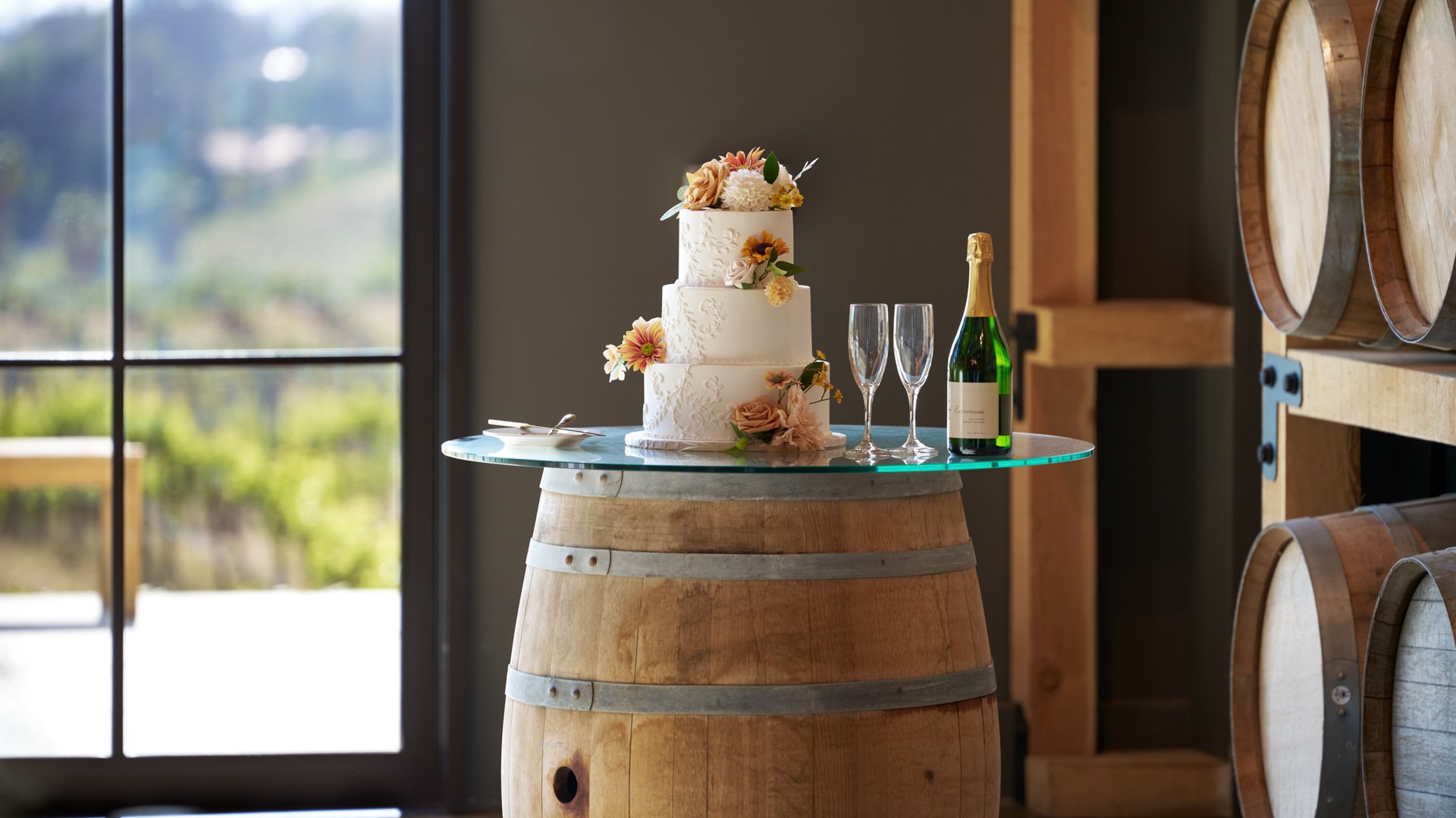 Elegant three-tier wedding cake with floral decorations displayed on a wine barrel table at Danza del Sol Winery in Temecula, California.