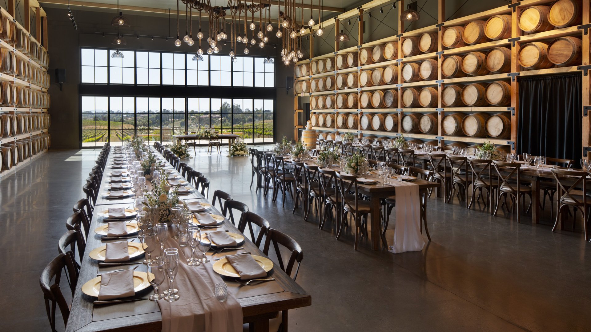 Elegant wedding reception setup in the Barrel Room at Danza del Sol Winery in Temecula, CA, with wine barrel walls, banquet tables, and natural light.